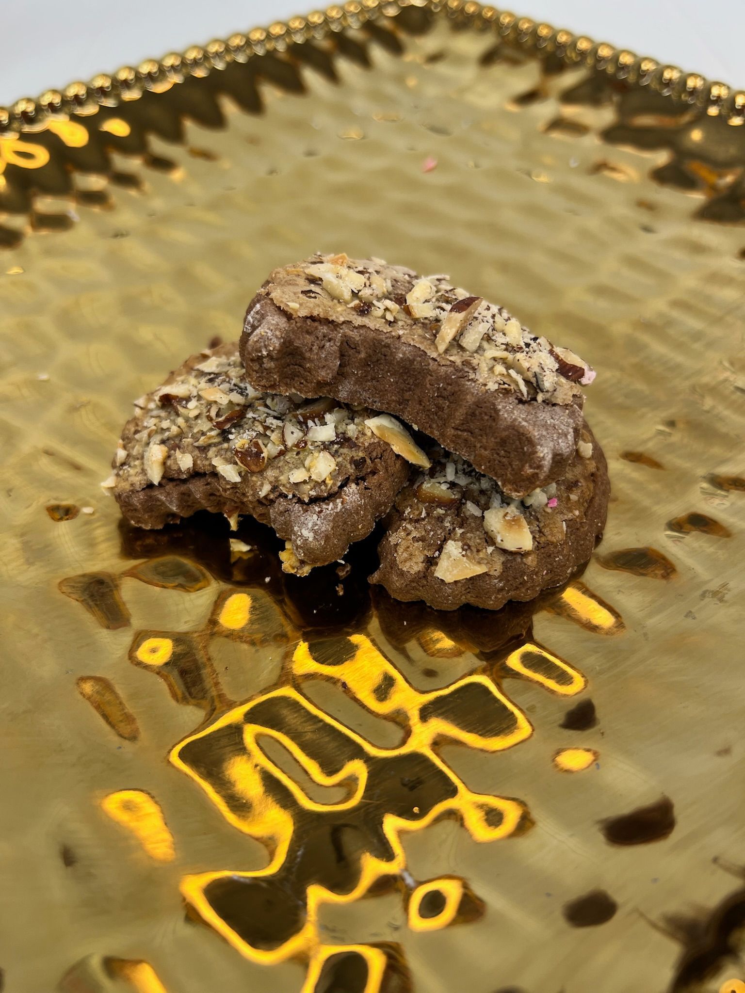 Cookies topped with nuts on a gold patterned plate.