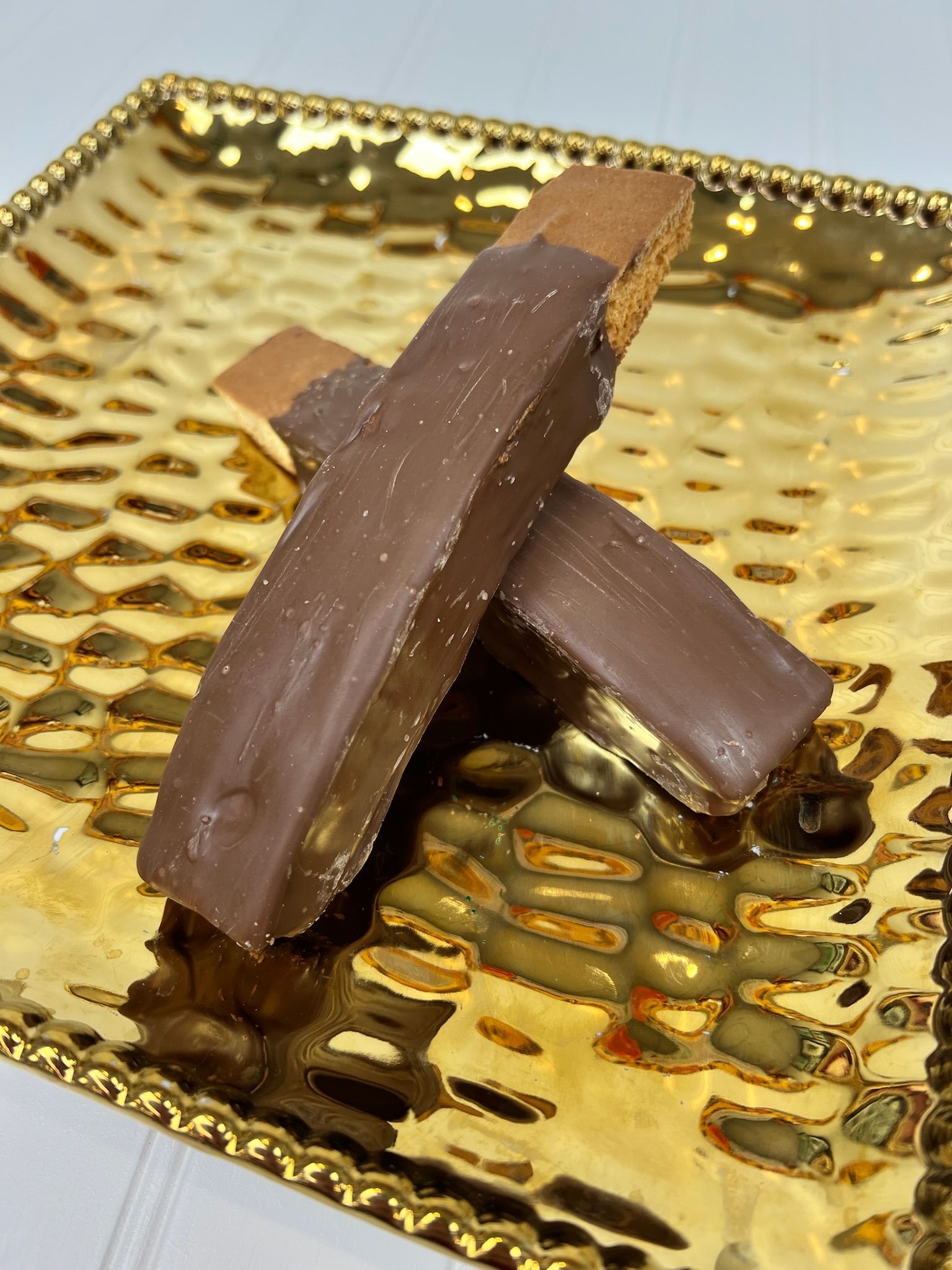 Two biscotti dipped in chocolate on a gold, textured tray.