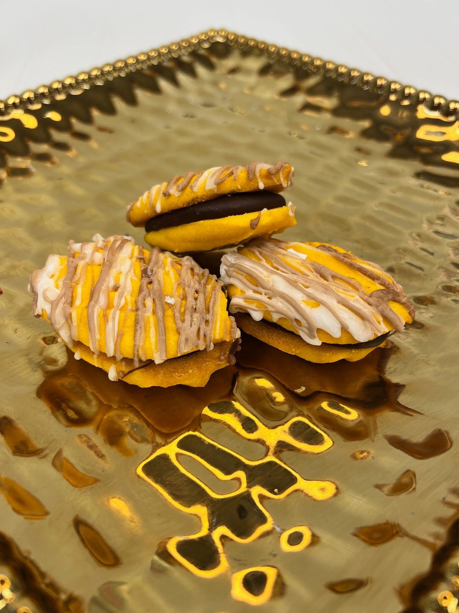 Three yellow, decorated sandwich cookies on a gold, patterned plate.