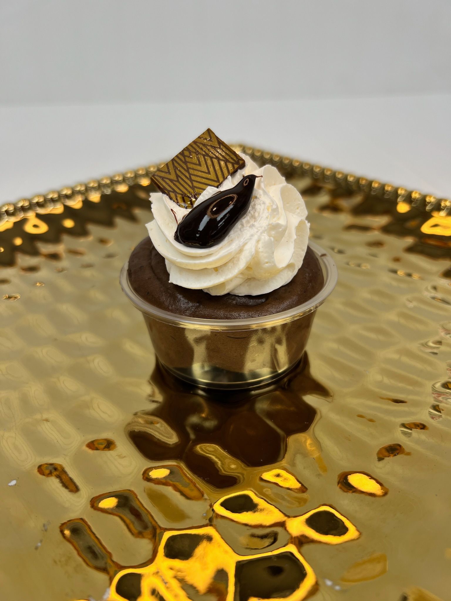 Chocolate cupcake with white frosting and chocolate garnish on gold tray.