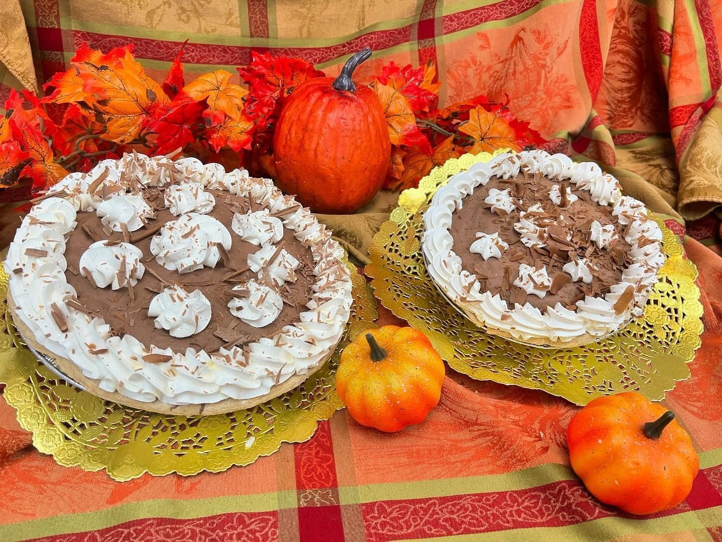 Two chocolate cream pies with whipped cream, pumpkins, and fall leaves.
