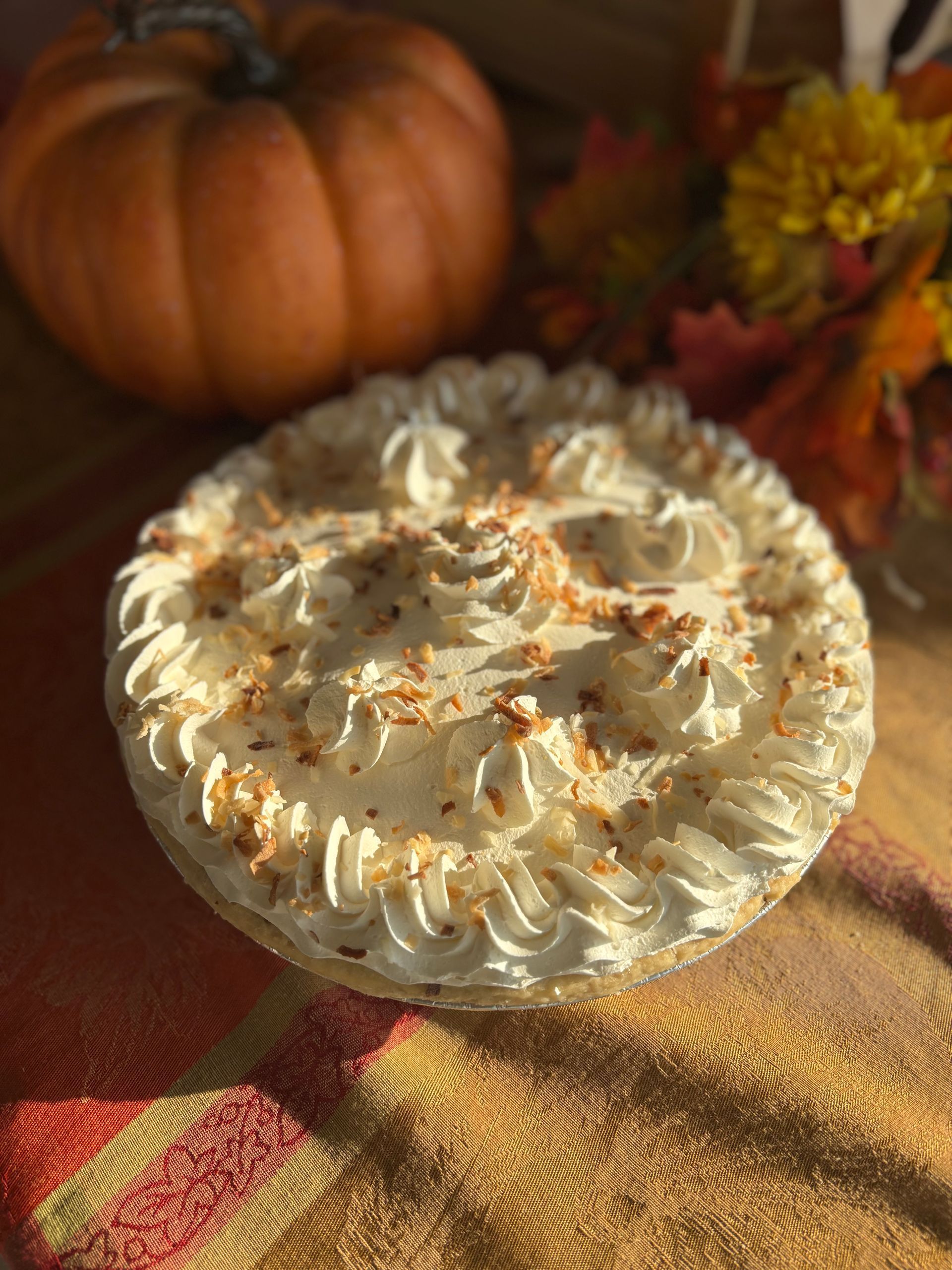 Pumpkin pie with whipped cream, autumn leaves and small pumpkin on orange plaid blanket.