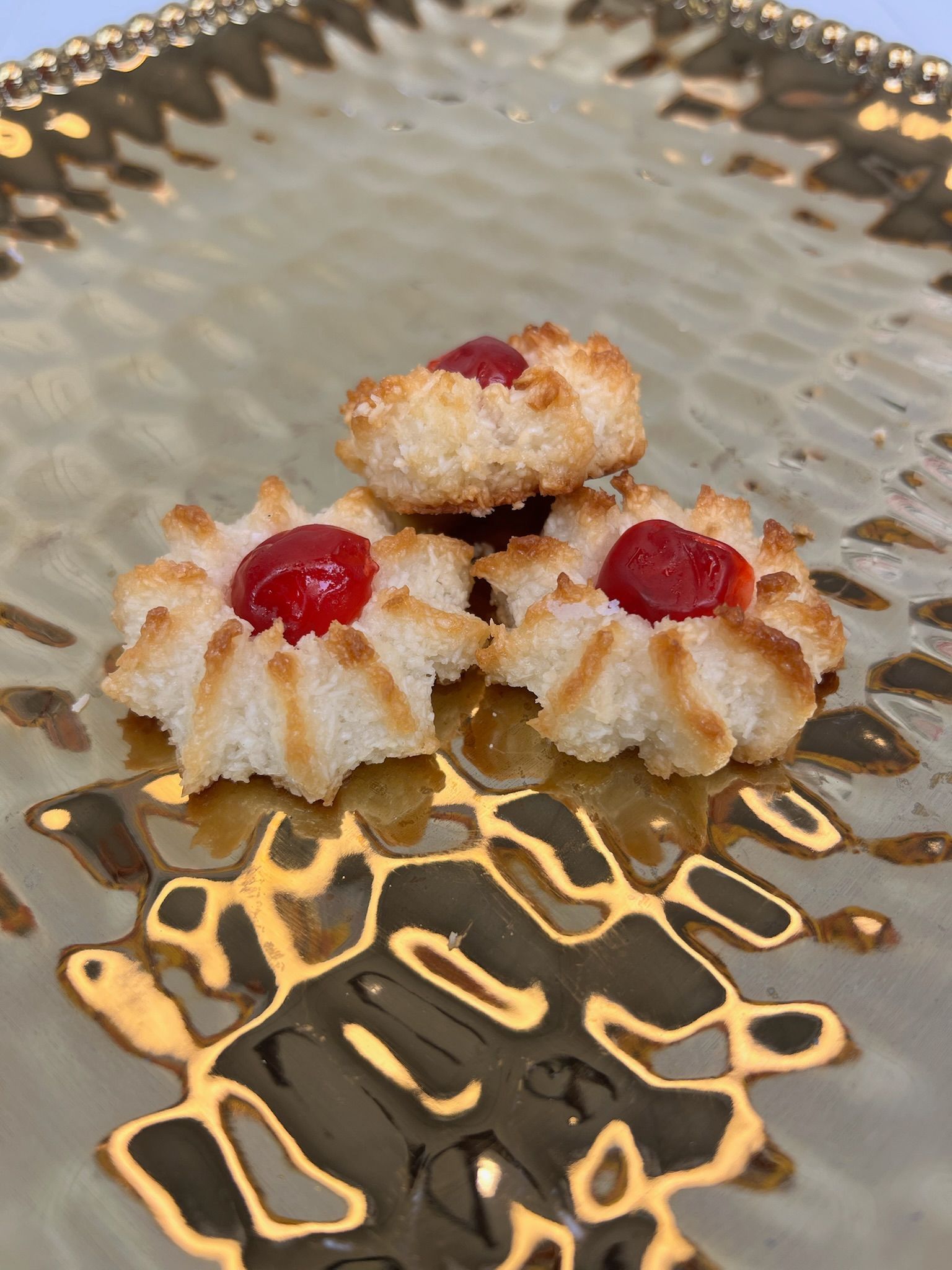 Coconut macaroons with red cherries on gold plate.