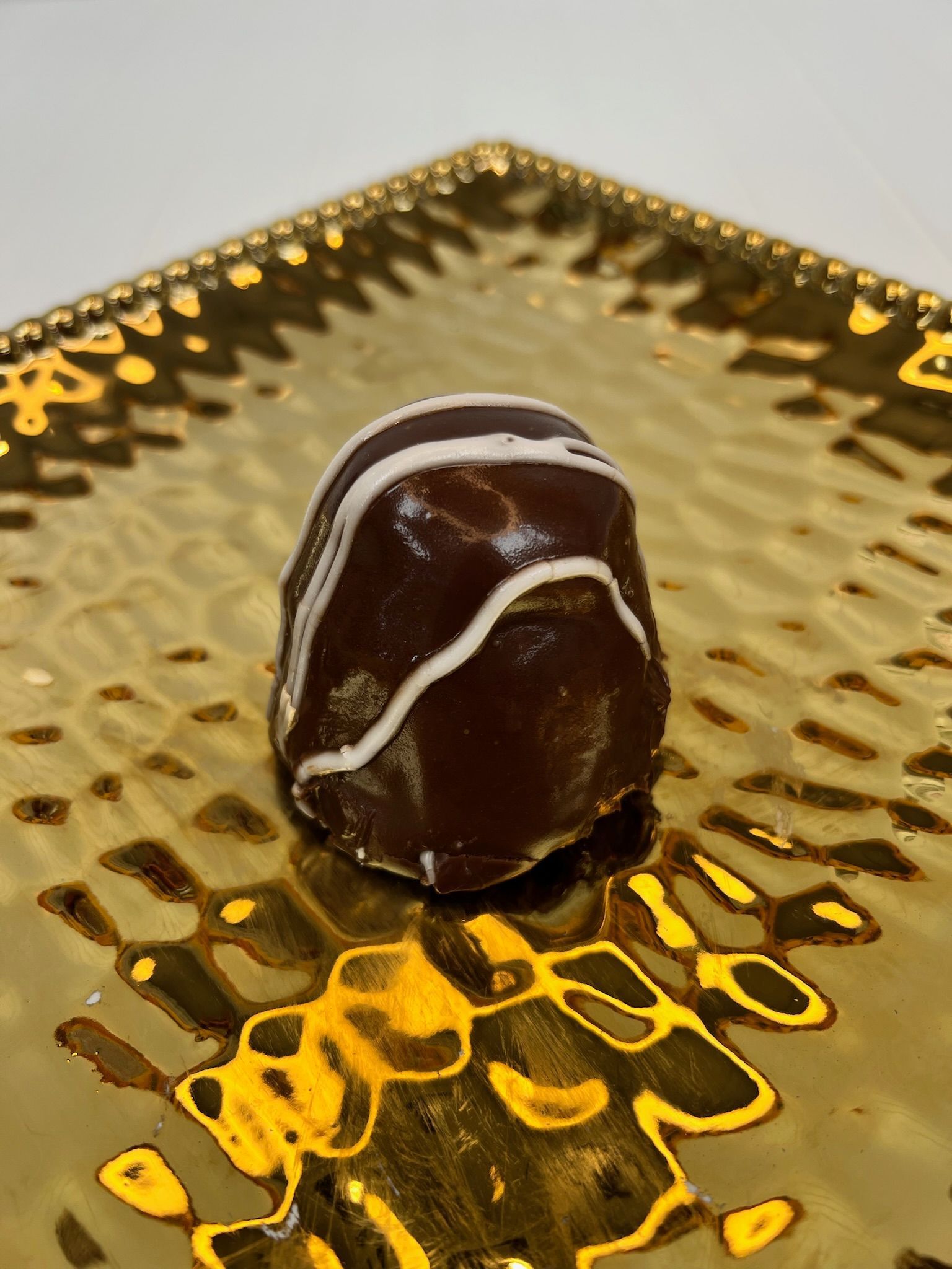 Chocolate truffle on a gold textured plate, drizzled with white lines.