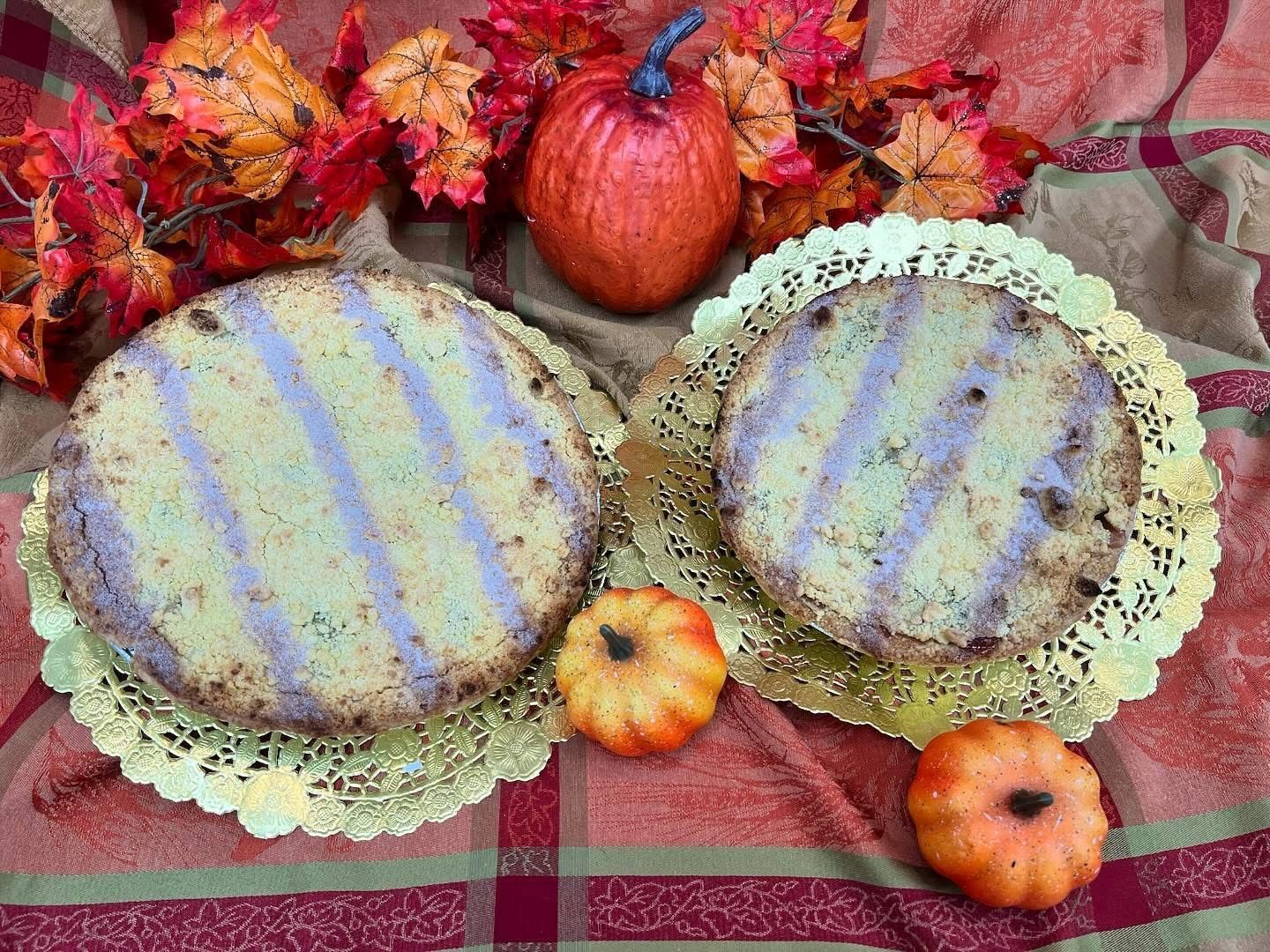 Two round cakes with grill marks on golden doilies, pumpkins and fall foliage.