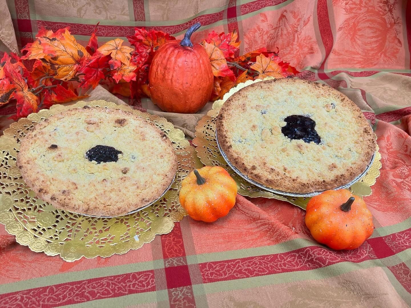 Two fruit pies on gold doilies, fall décor with pumpkins and leaves, plaid fabric.