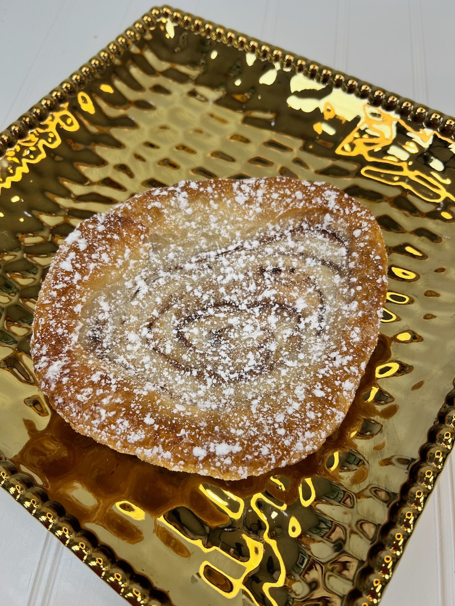 Pastry dusted with powdered sugar on a gold, textured plate.