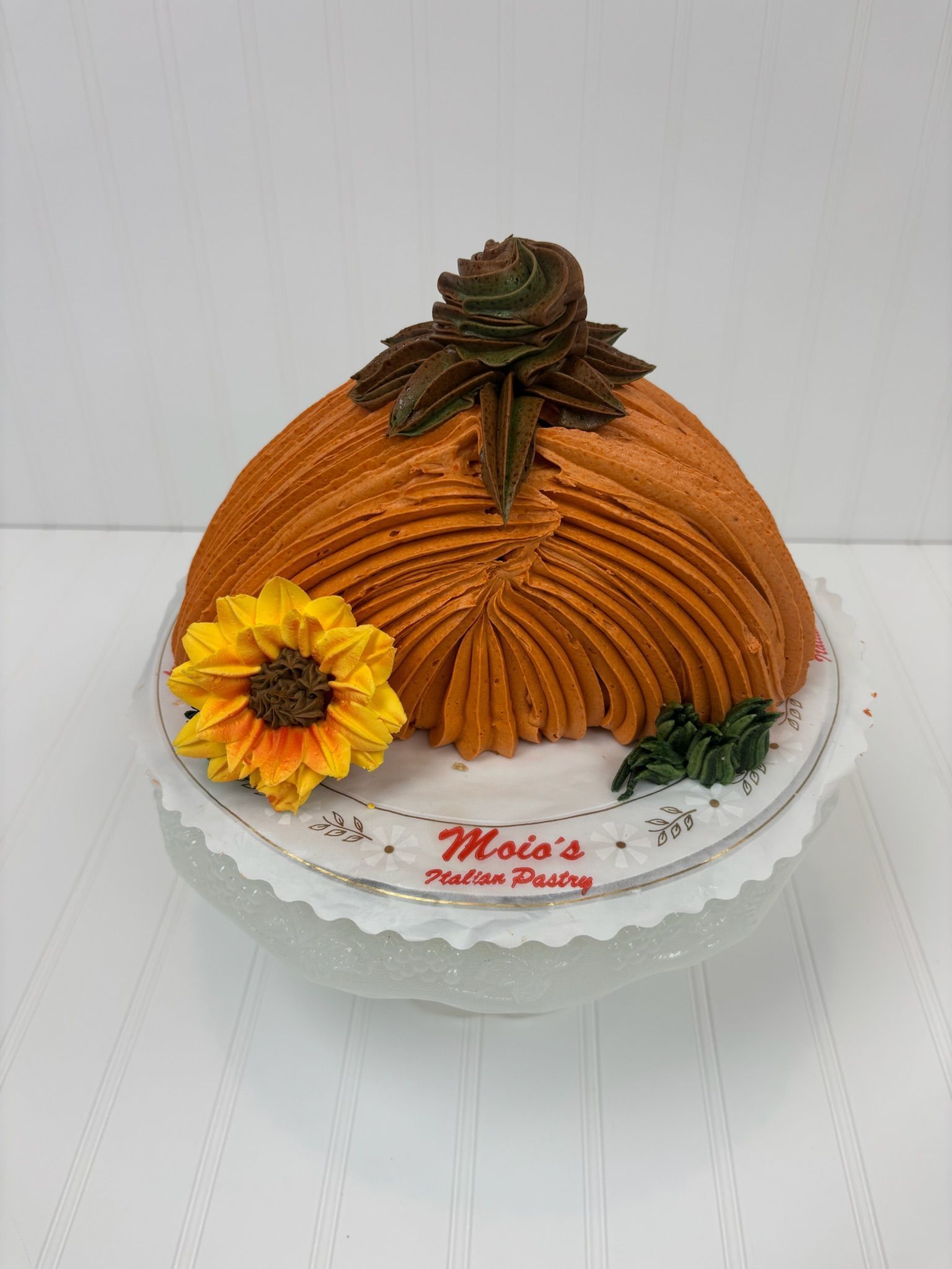 Orange buttercream pumpkin cake decorated with a sunflower on a white cake stand.