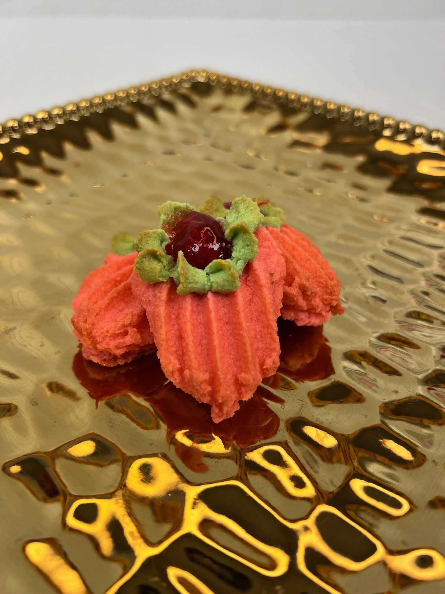 Three pink floral cookies with green icing and a cherry on a gold plate.