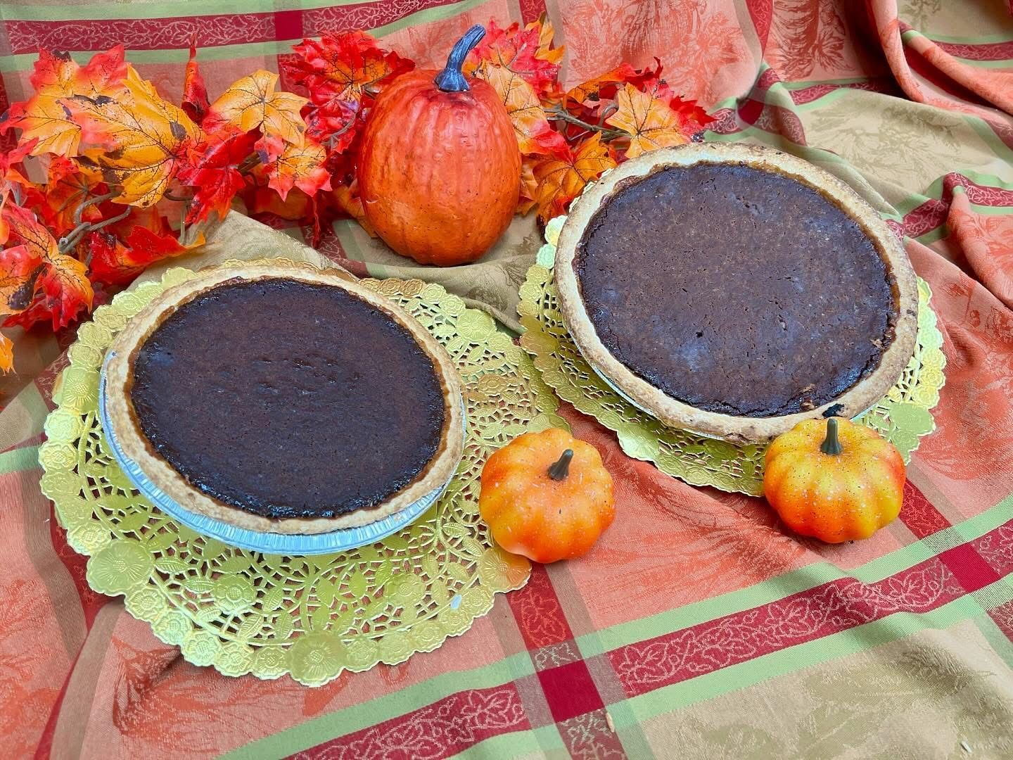 Two pumpkin pies on gold doilies, surrounded by pumpkins and fall leaves on a plaid tablecloth.