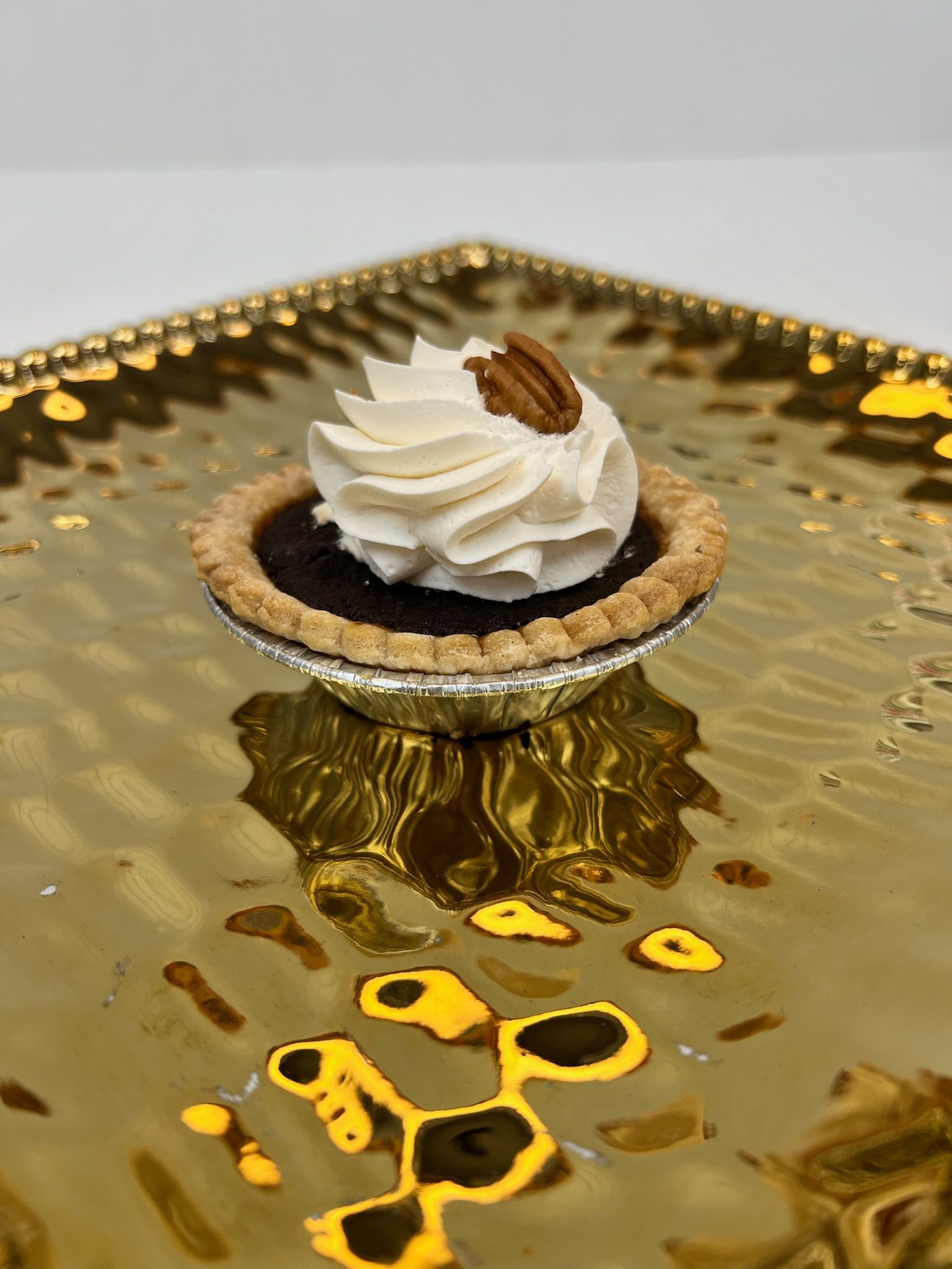 Mini chocolate pecan pie with whipped cream and a pecan on a gold tray.