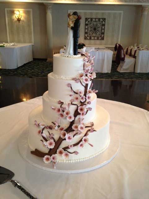 Four-tiered white wedding cake with floral accents and a bride and groom topper, set on a table.