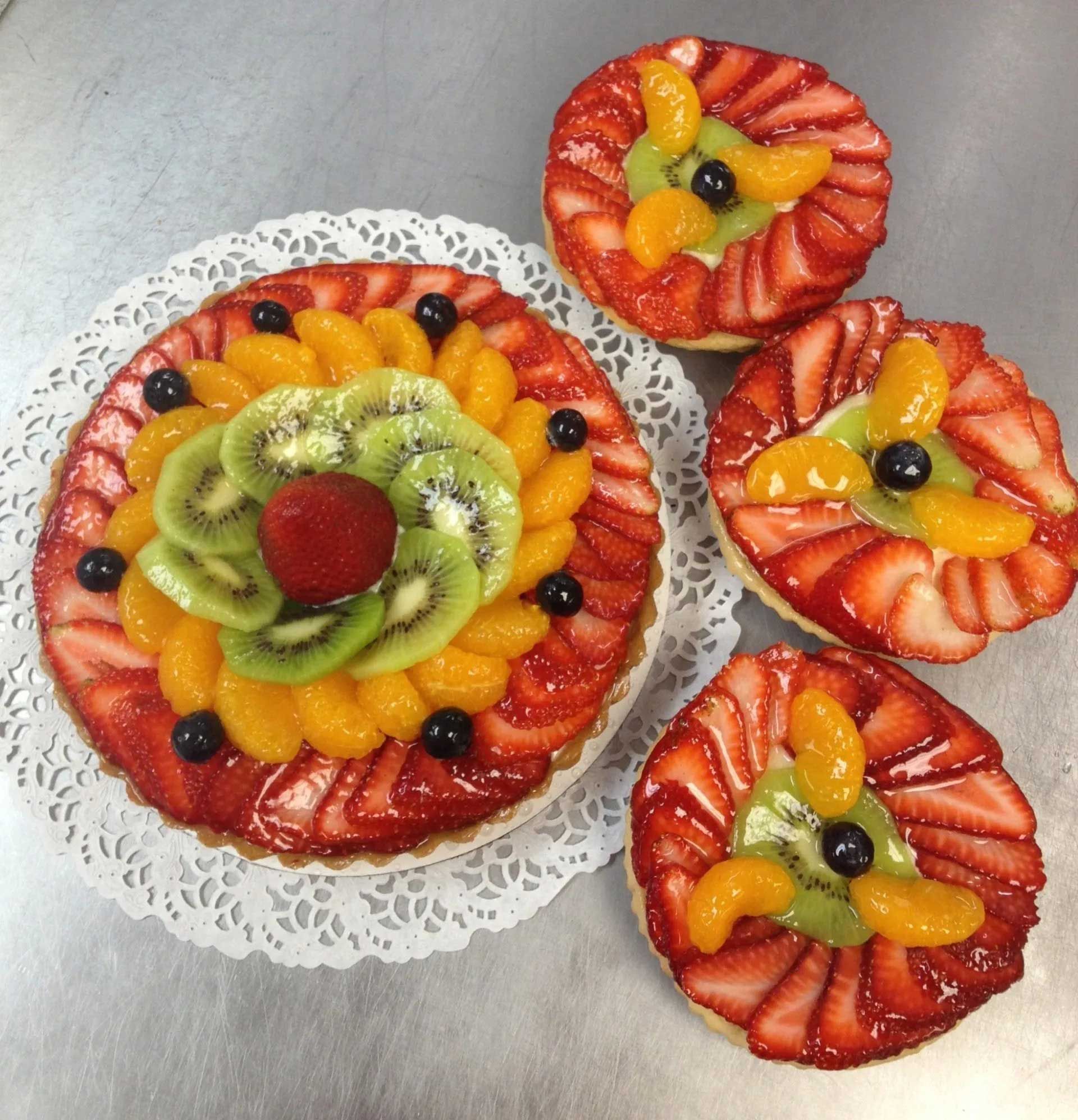 Fruit tarts with strawberries, kiwi, and mandarin oranges arranged in a decorative pattern on a white doily.