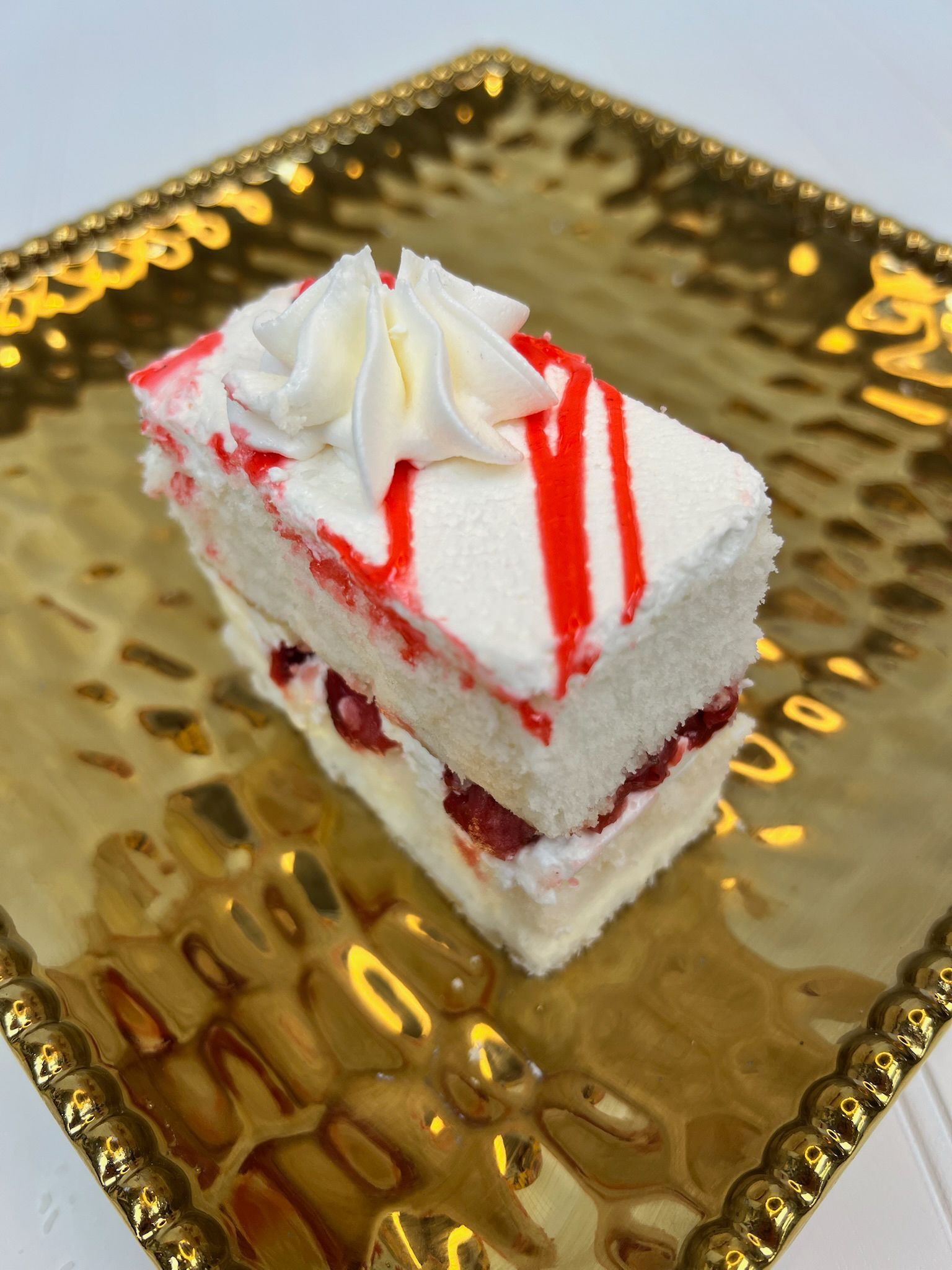 Slice of cake with white frosting, red stripes, and whipped cream on a gold platter.