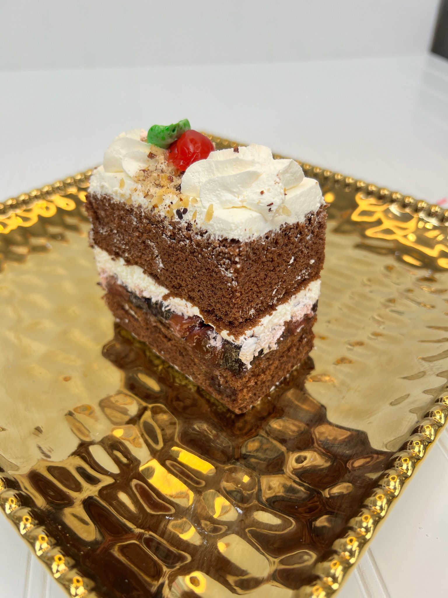 Slice of chocolate cake with white frosting and a cherry on a gold platter.