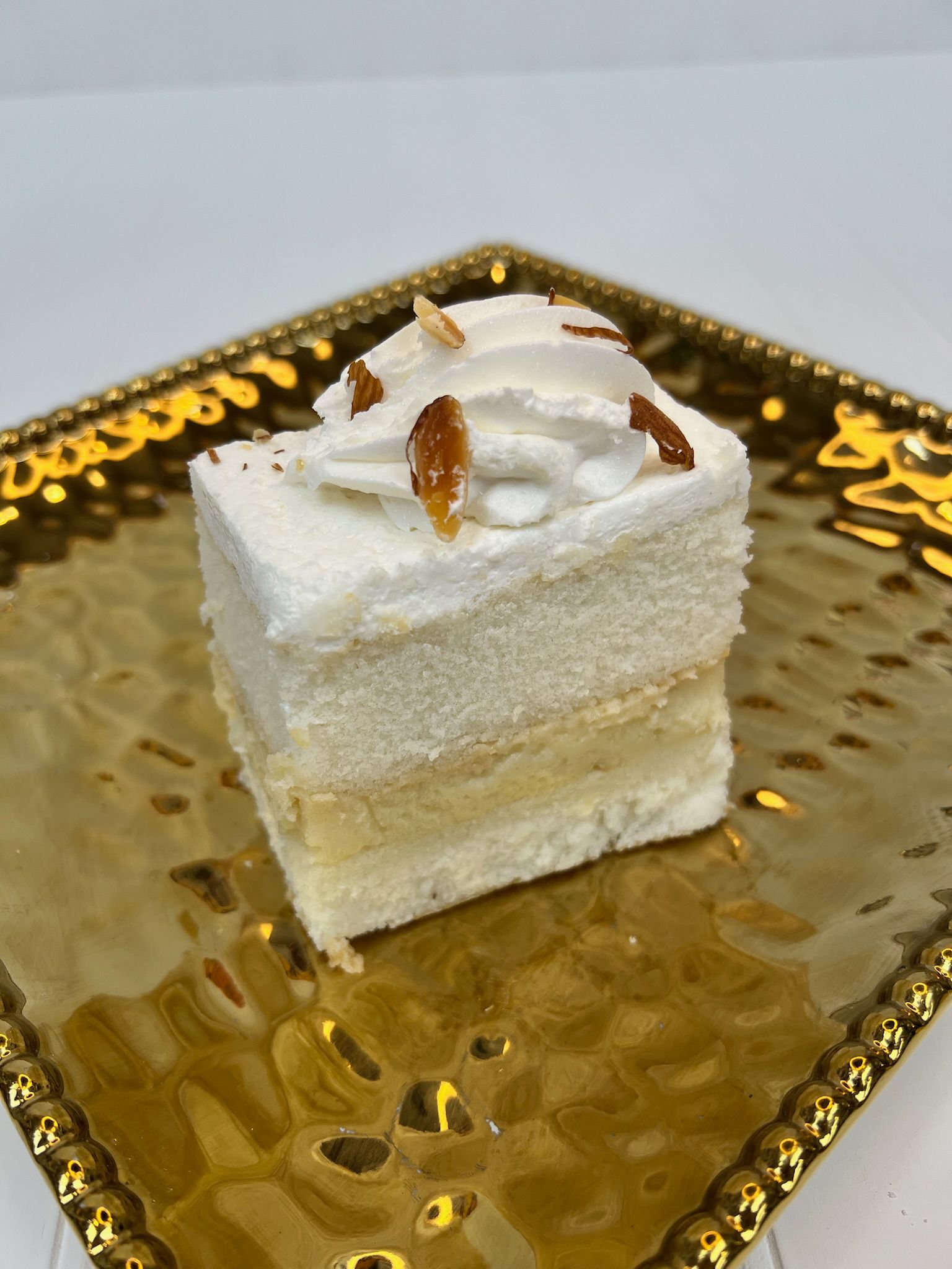 Square layered cake on a gold plate, topped with whipped cream and toasted coconut flakes.