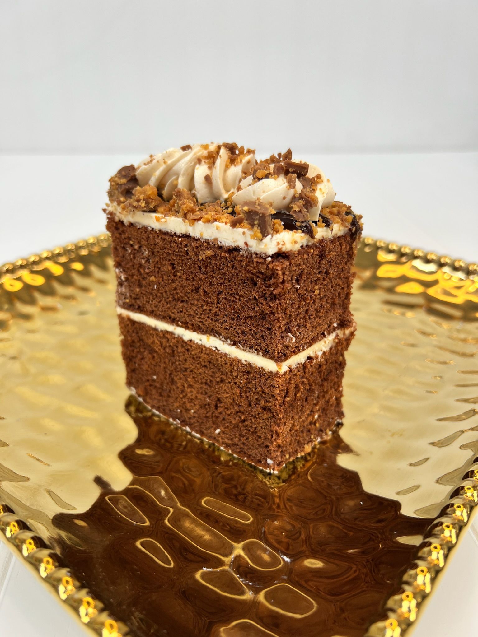 Chocolate cake slice on a gold platter, topped with frosting and crumble.