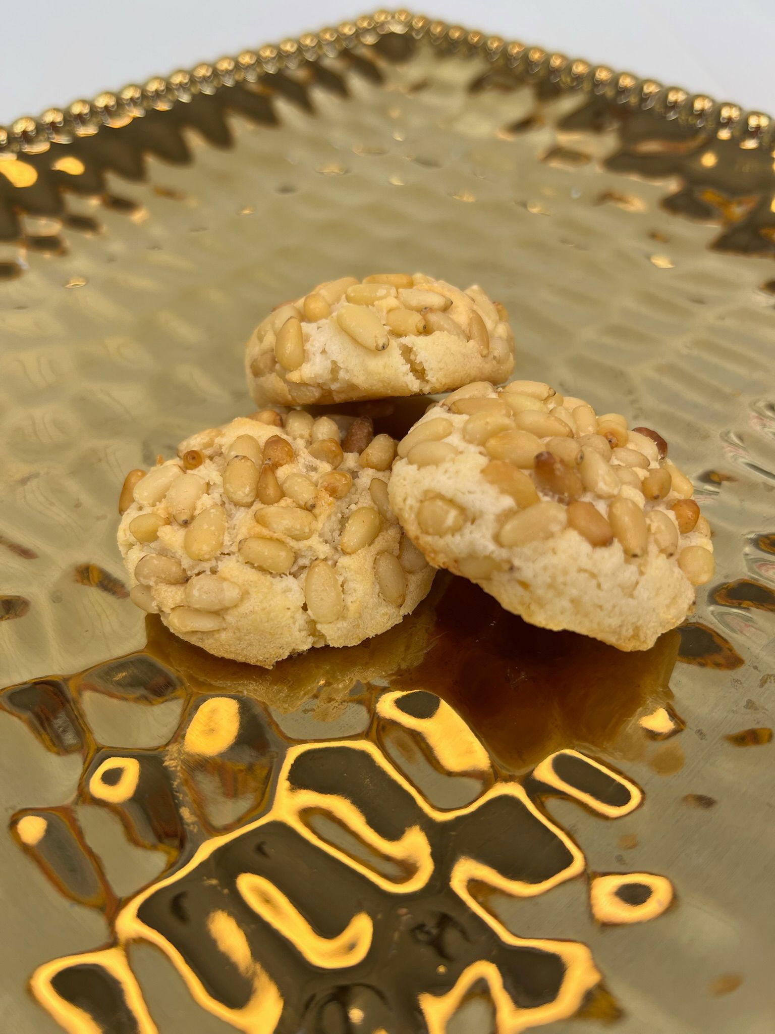 Cookies topped with pine nuts on a gold textured plate.