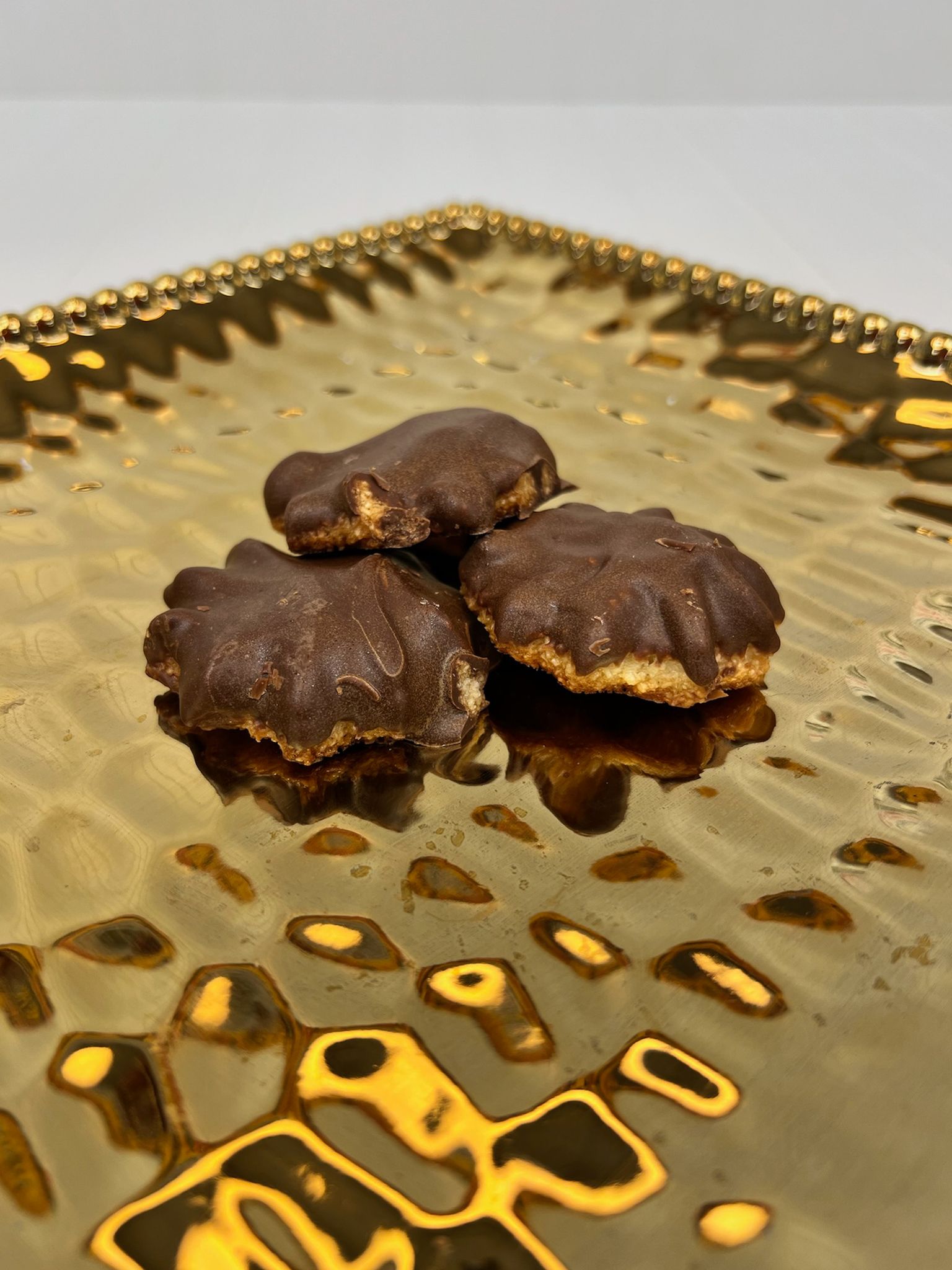 Three chocolate-covered cookies on a textured gold plate.