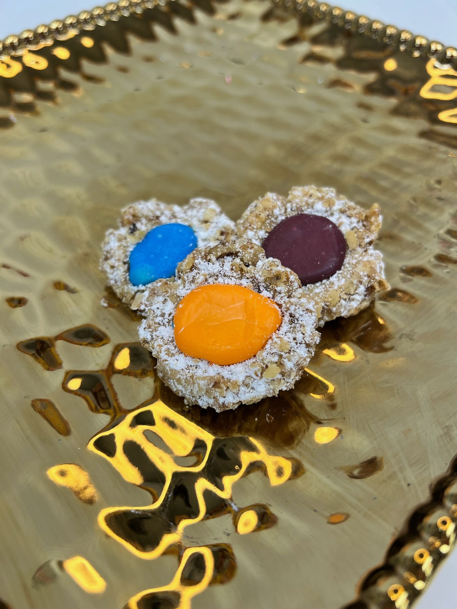 Three oatmeal cookies with colorful candy centers on a gold platter.