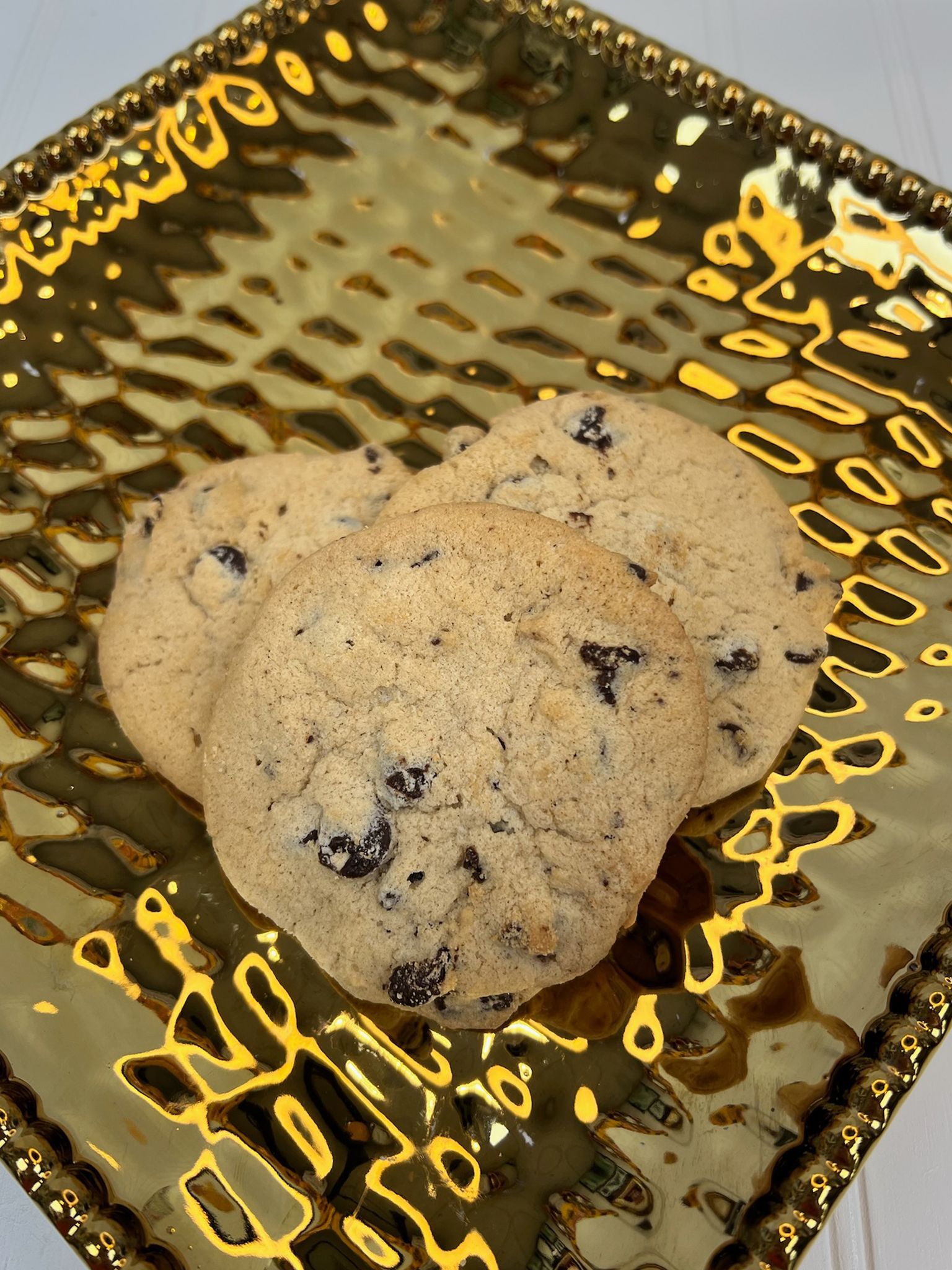 Three chocolate chip cookies on a gold, textured plate.