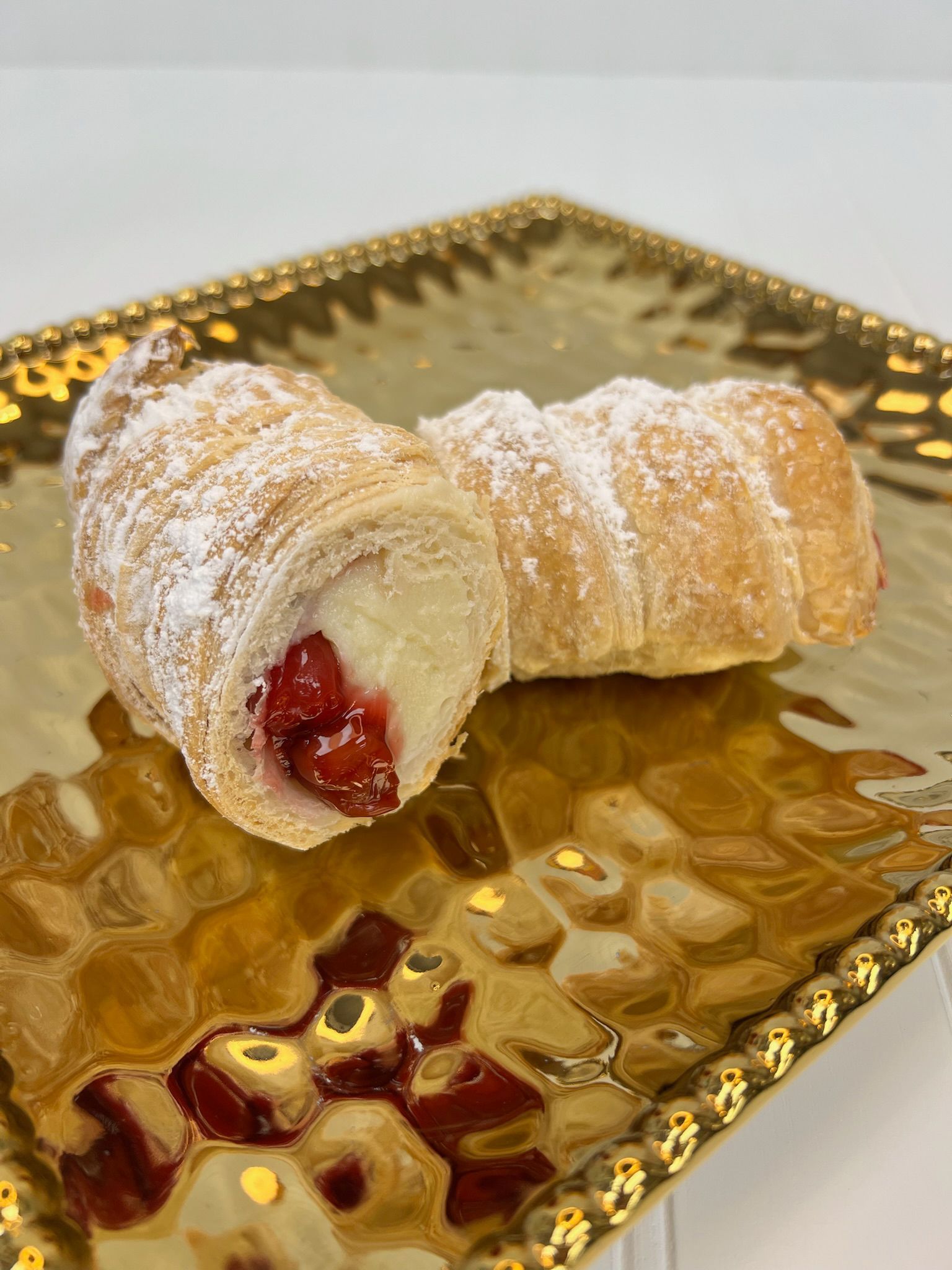 Two cream horns, filled with cream and cherries, dusted with powdered sugar, on a gold tray.