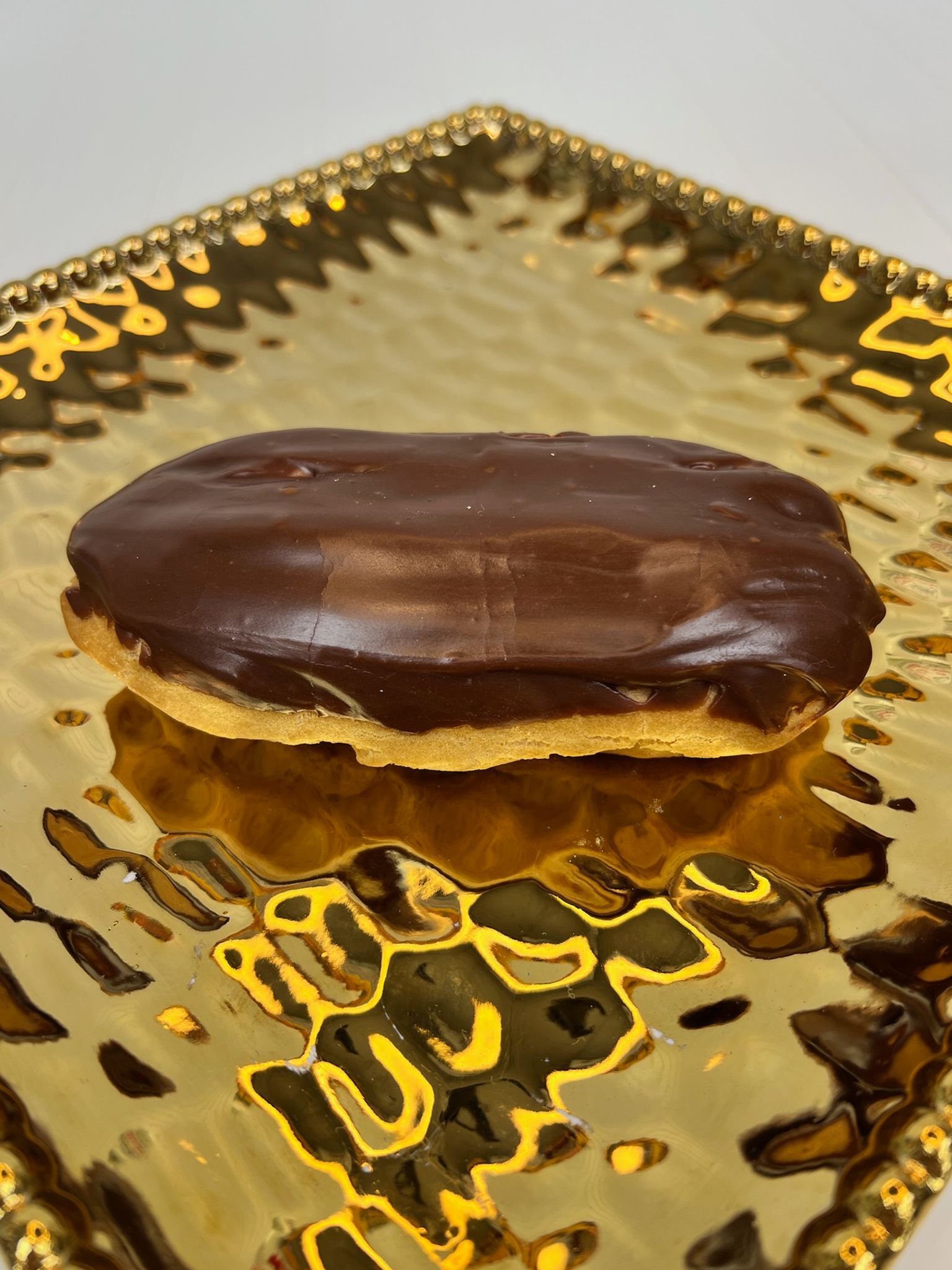 Chocolate-covered éclair on a gold, textured platter.