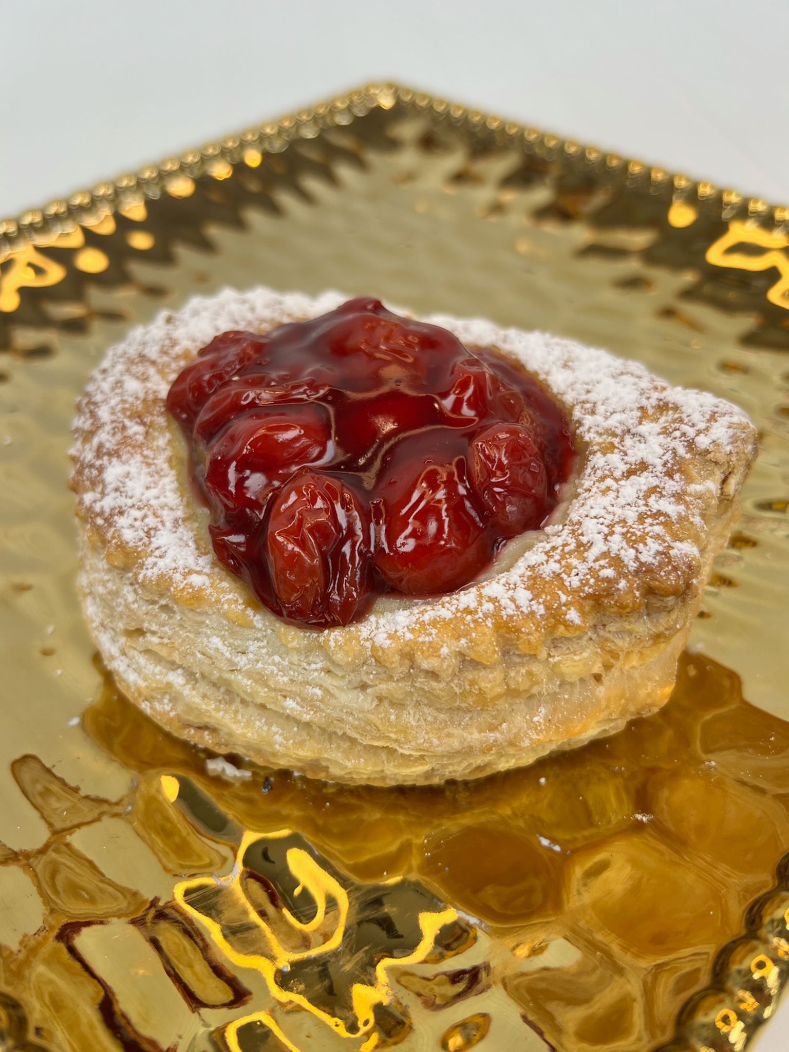 Pastry with cherries on a gold plate, dusted with powdered sugar.