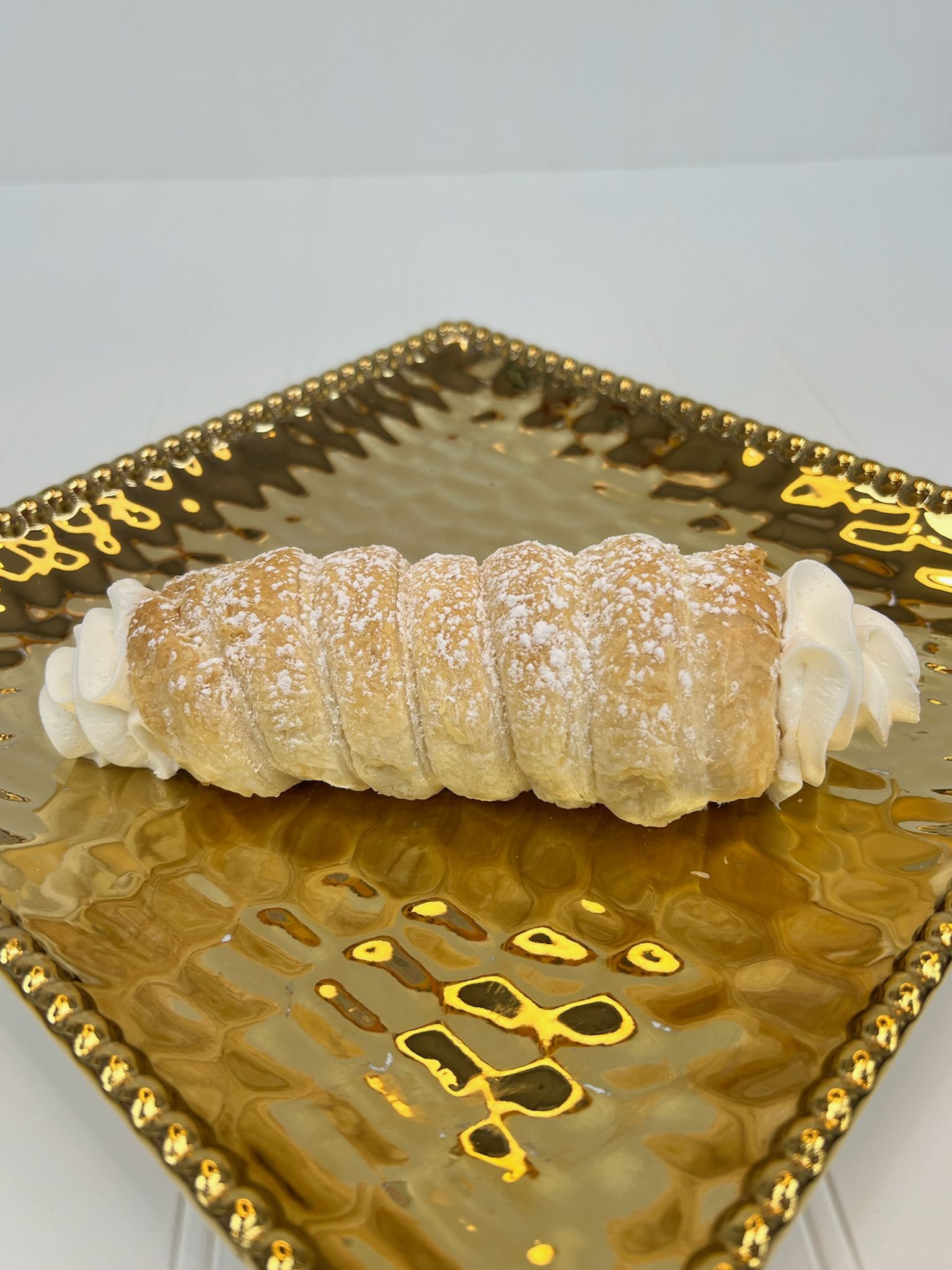 Cannoli on a gold, square, textured plate, dusted with powdered sugar and whipped cream.
