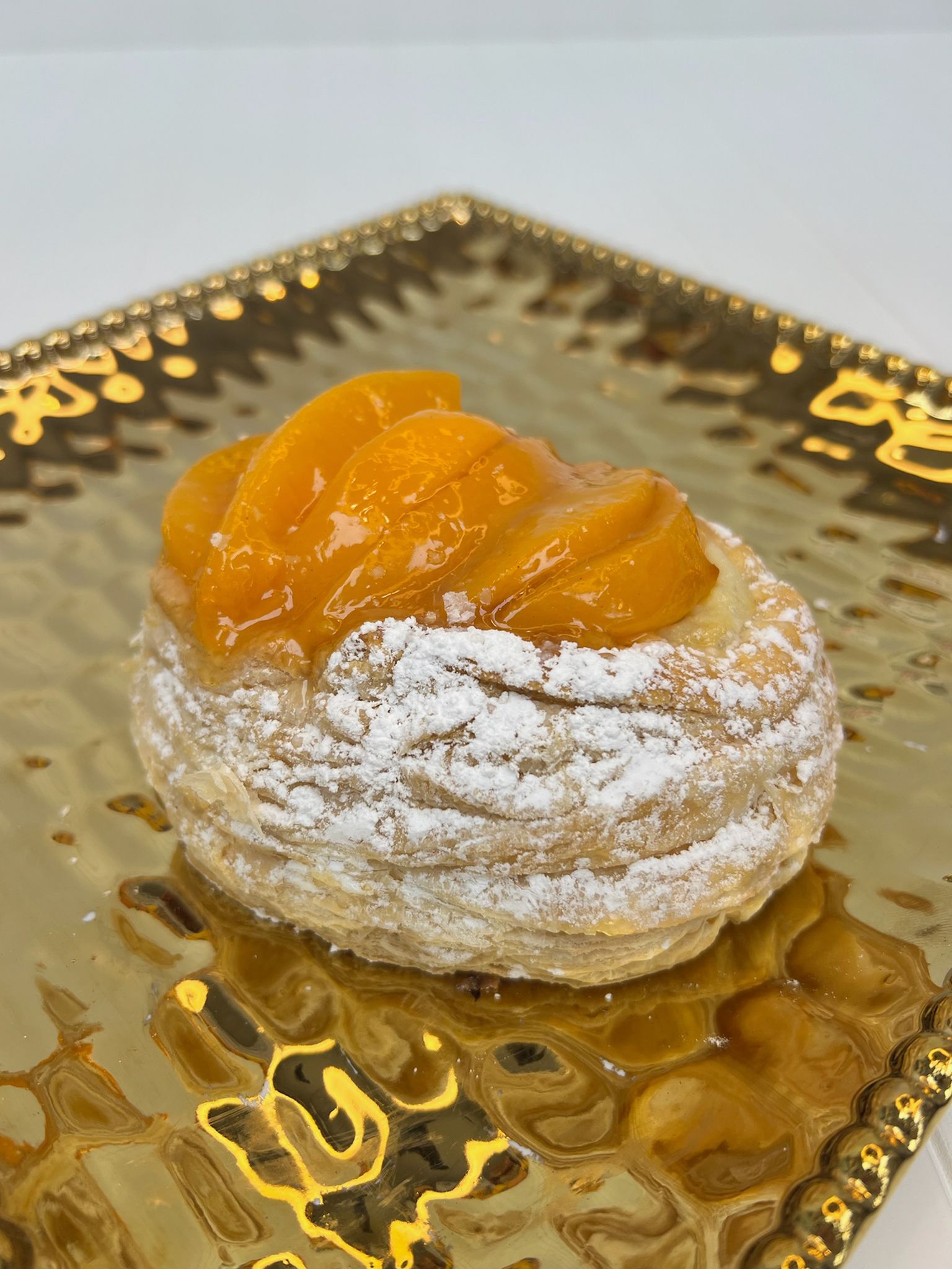 Pastry topped with glazed peach slices, dusted with powdered sugar, on a gold plate.