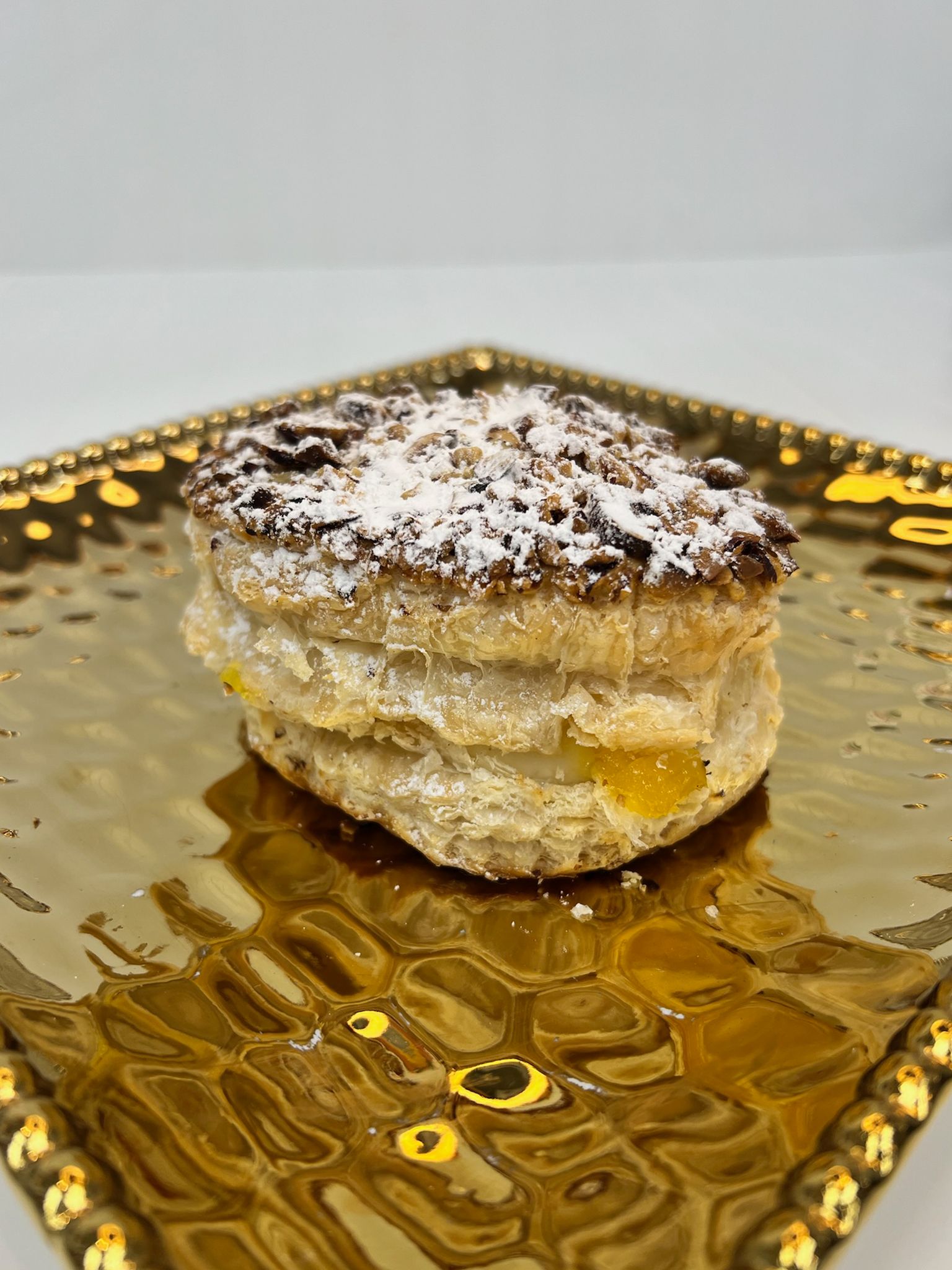 Pastry with yellow filling, topped with dark crumbles and powdered sugar, on a gold plate.
