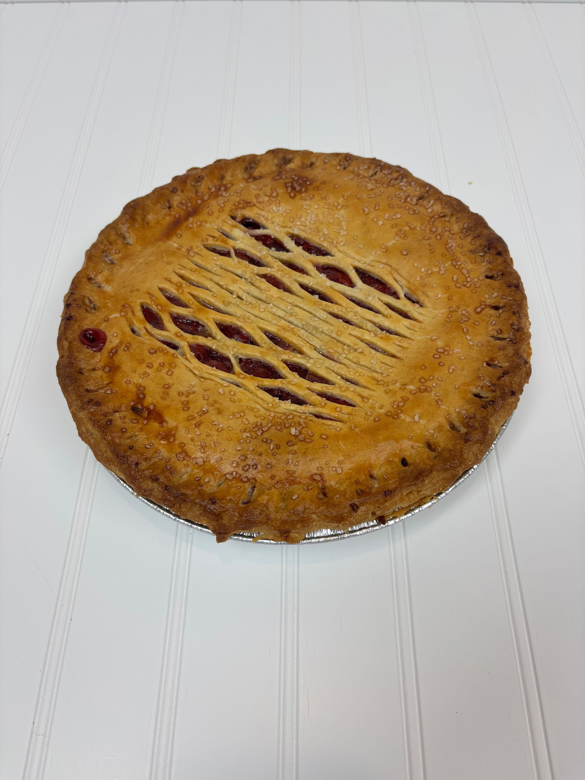 Cherry pie with lattice crust, golden-brown, on a white surface.