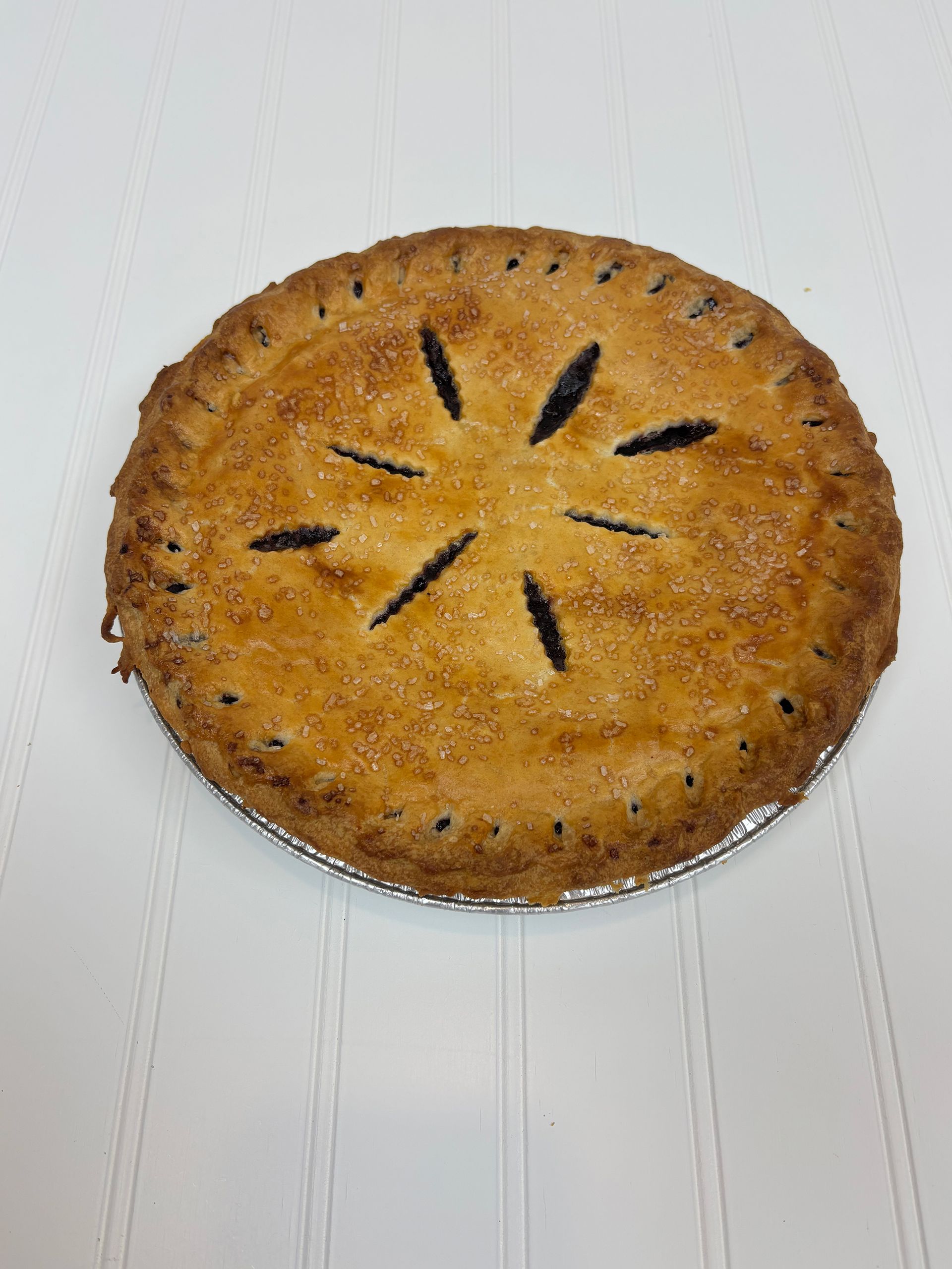 Baked pie with a golden crust, decorative slits, and sugar crystals on a white surface.