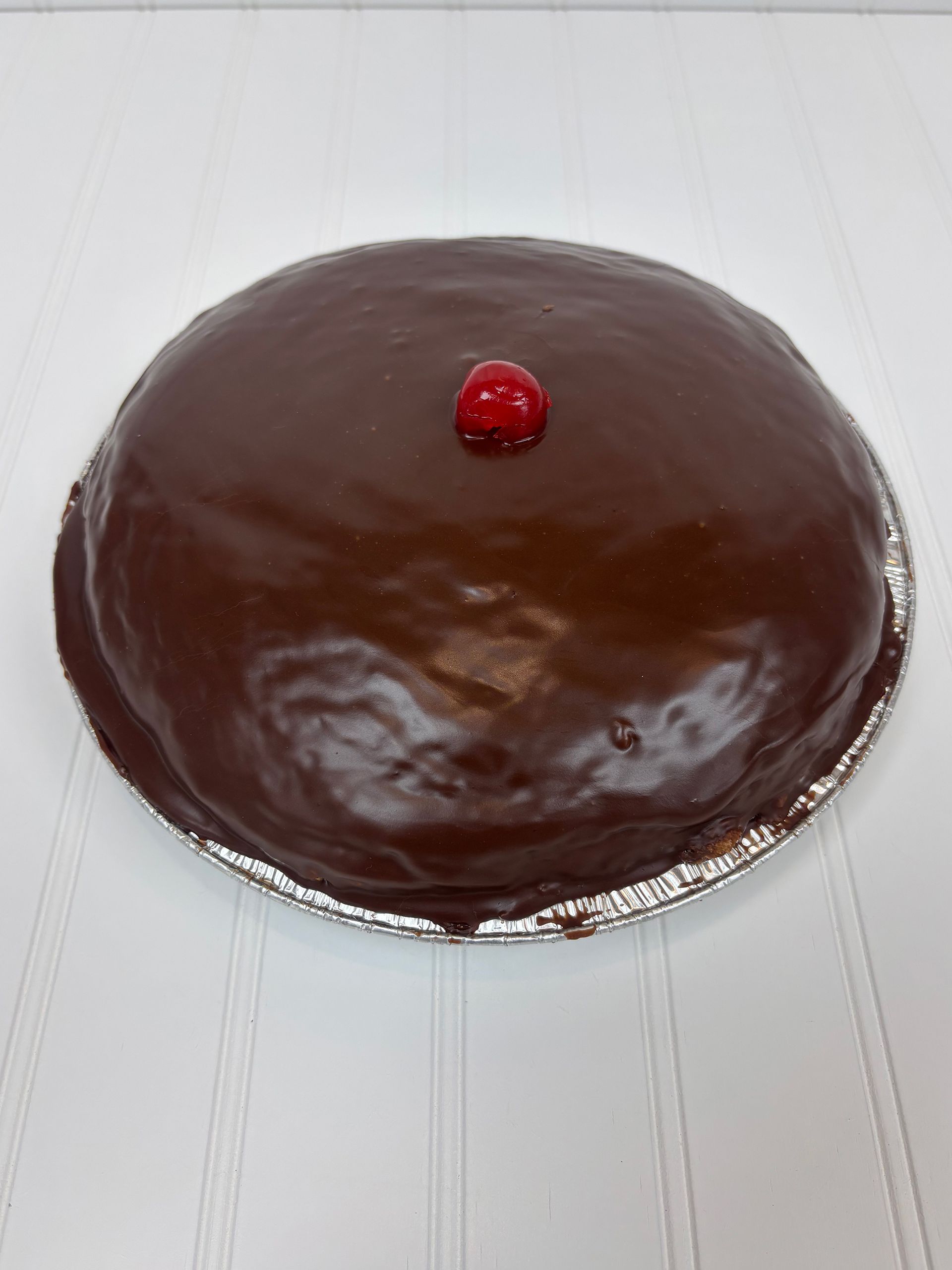 Chocolate cake with shiny frosting and a cherry on top, in a silver tin.