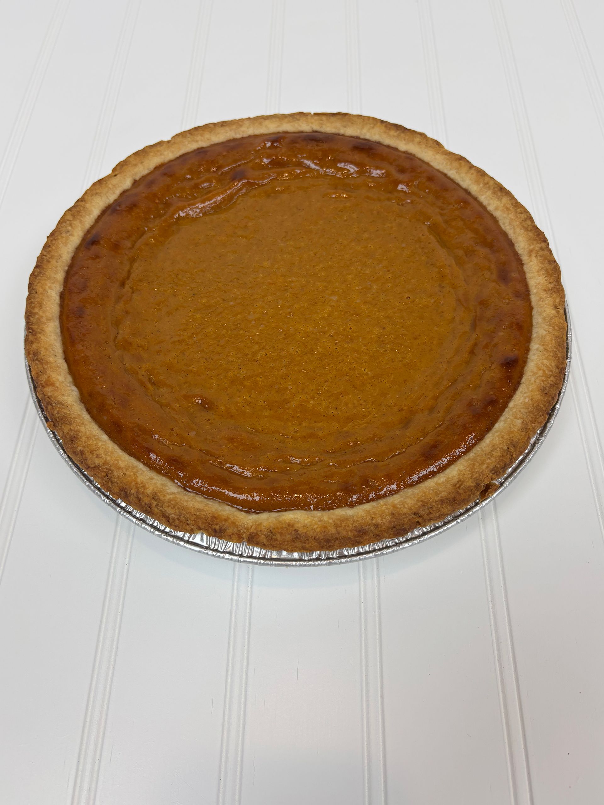 Pumpkin pie in a foil pan on a white surface.