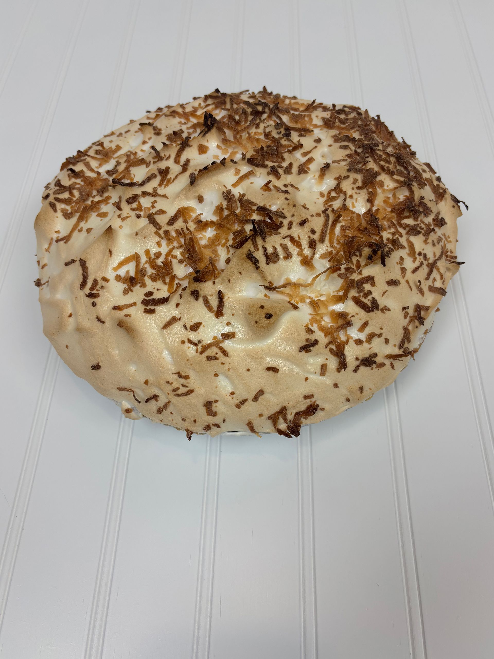Round, white pastry topped with toasted coconut flakes, on a white surface.