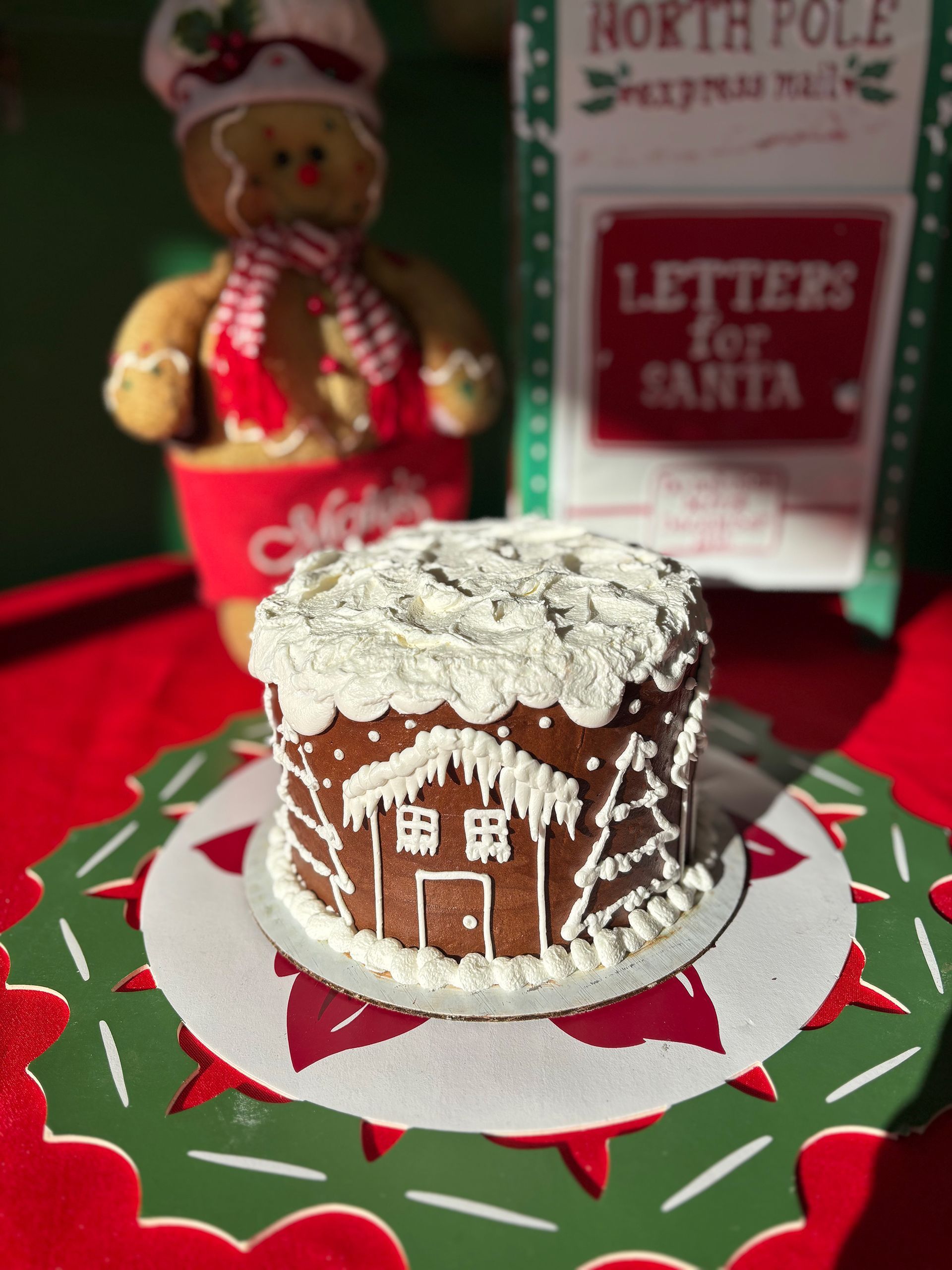 Gingerbread house cake on a holiday-themed plate with a gingerbread man and