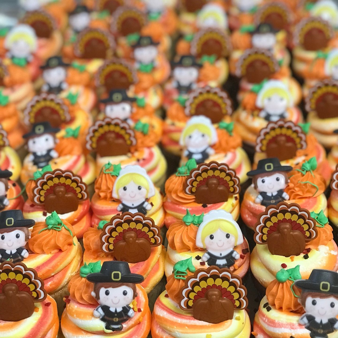 Thanksgiving cupcakes with orange frosting, pilgrim figurines, and turkey decorations.