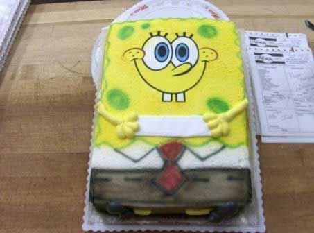 SpongeBob SquarePants cake with yellow frosting, smiling face, holding a sign, on a wooden table.
