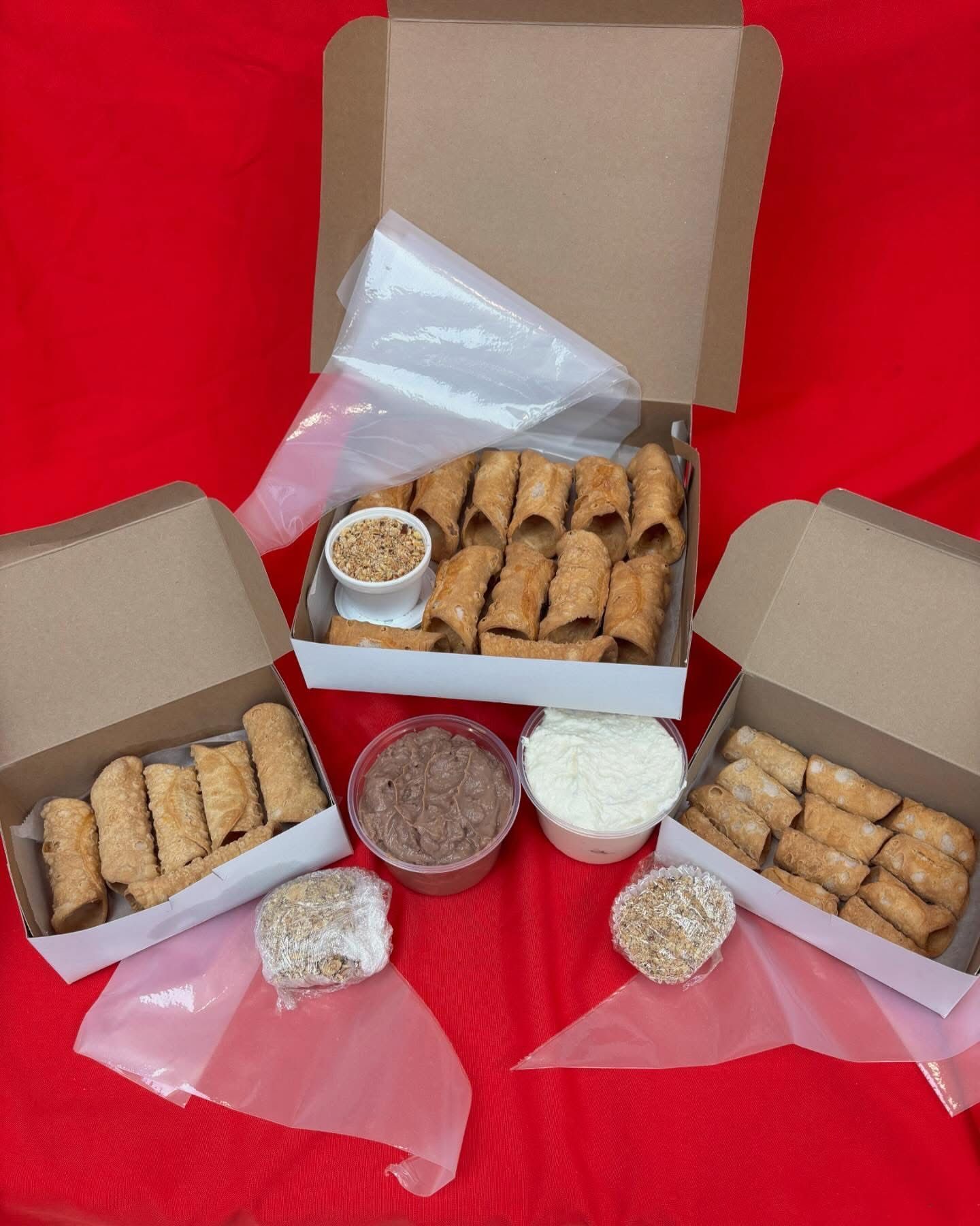 Three boxes of cannoli pastries with fillings and toppings on red surface.