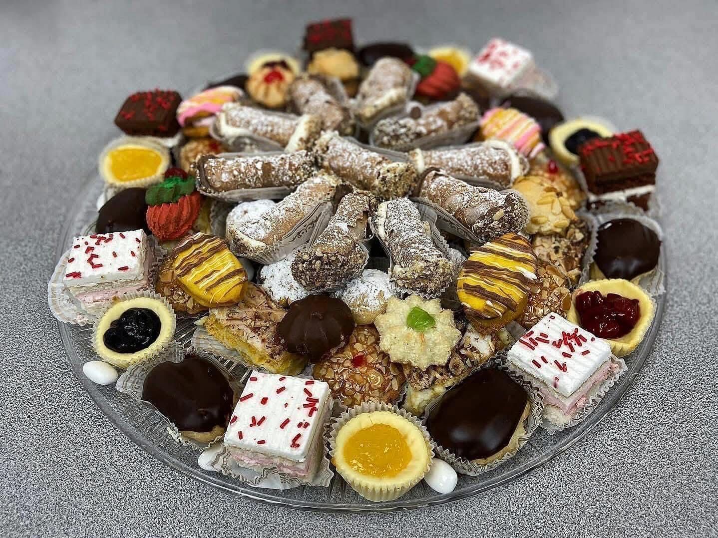 Assorted pastries on a clear, round platter; including cannoli, small cakes, and tarts.