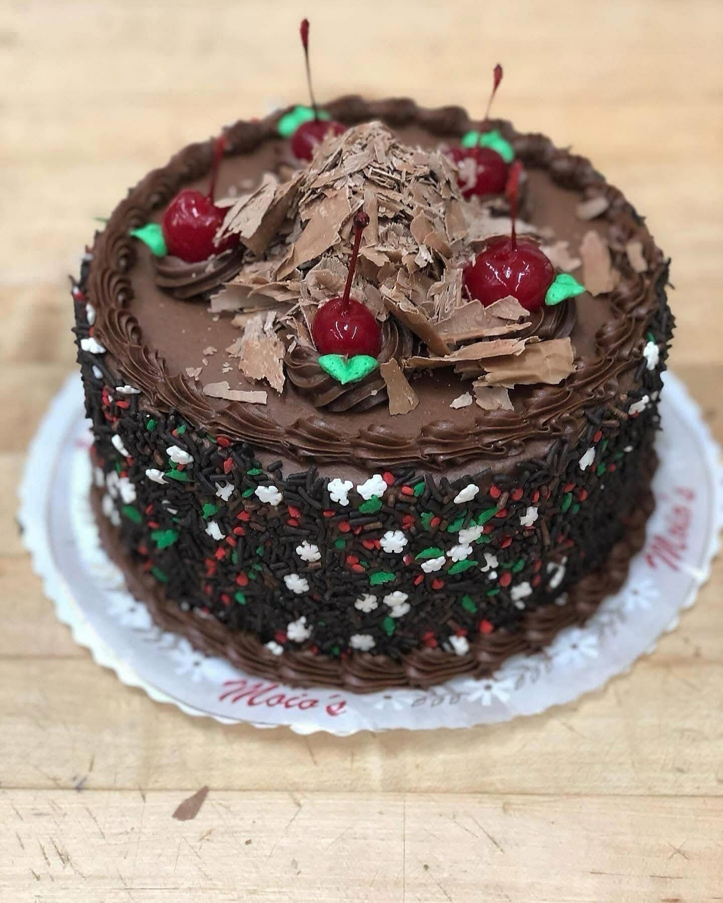 Chocolate cake decorated with cherries, chocolate shavings, and sprinkles.