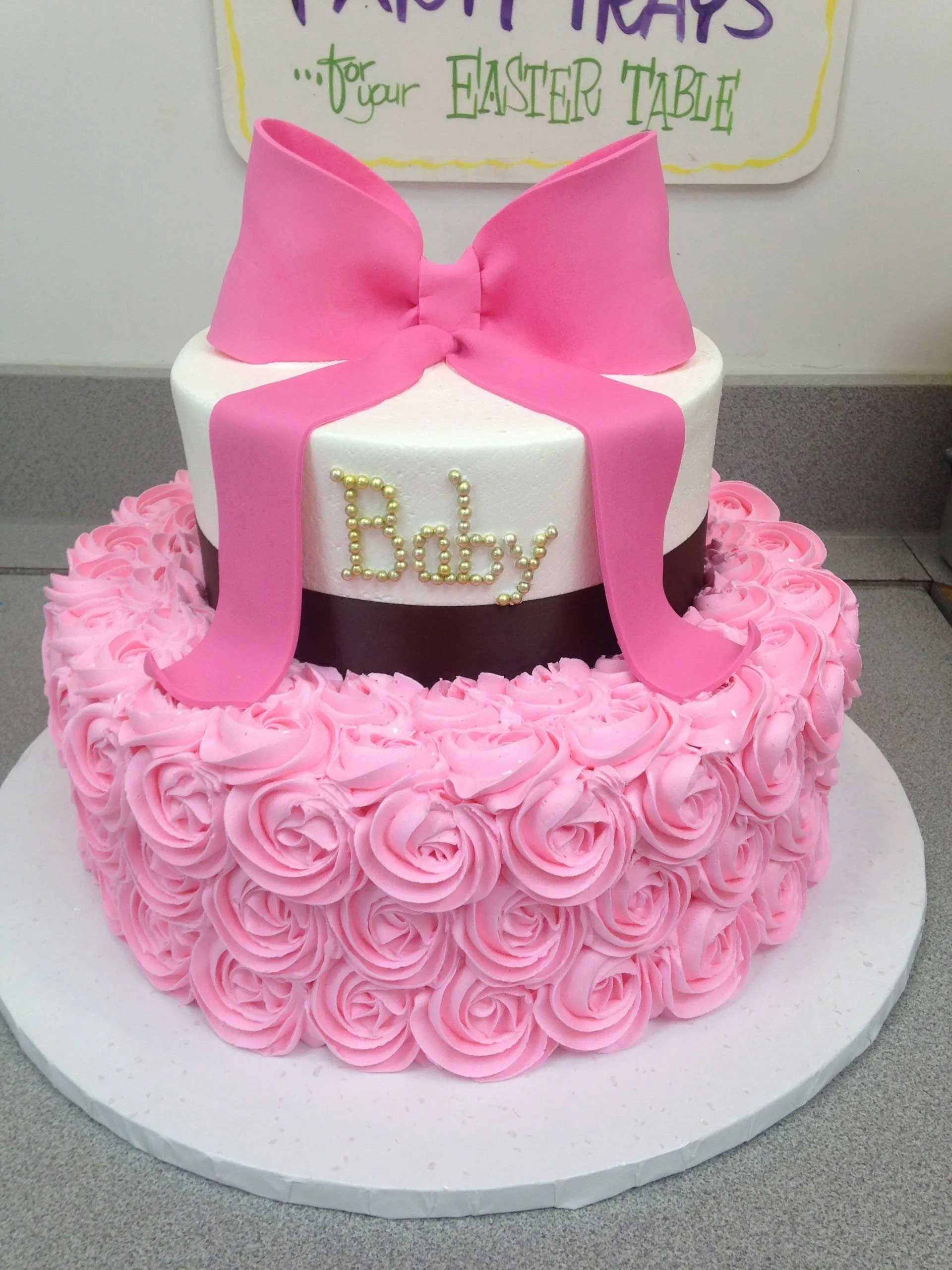Two-tiered pink baby shower cake with rosette frosting and a large pink bow on top.