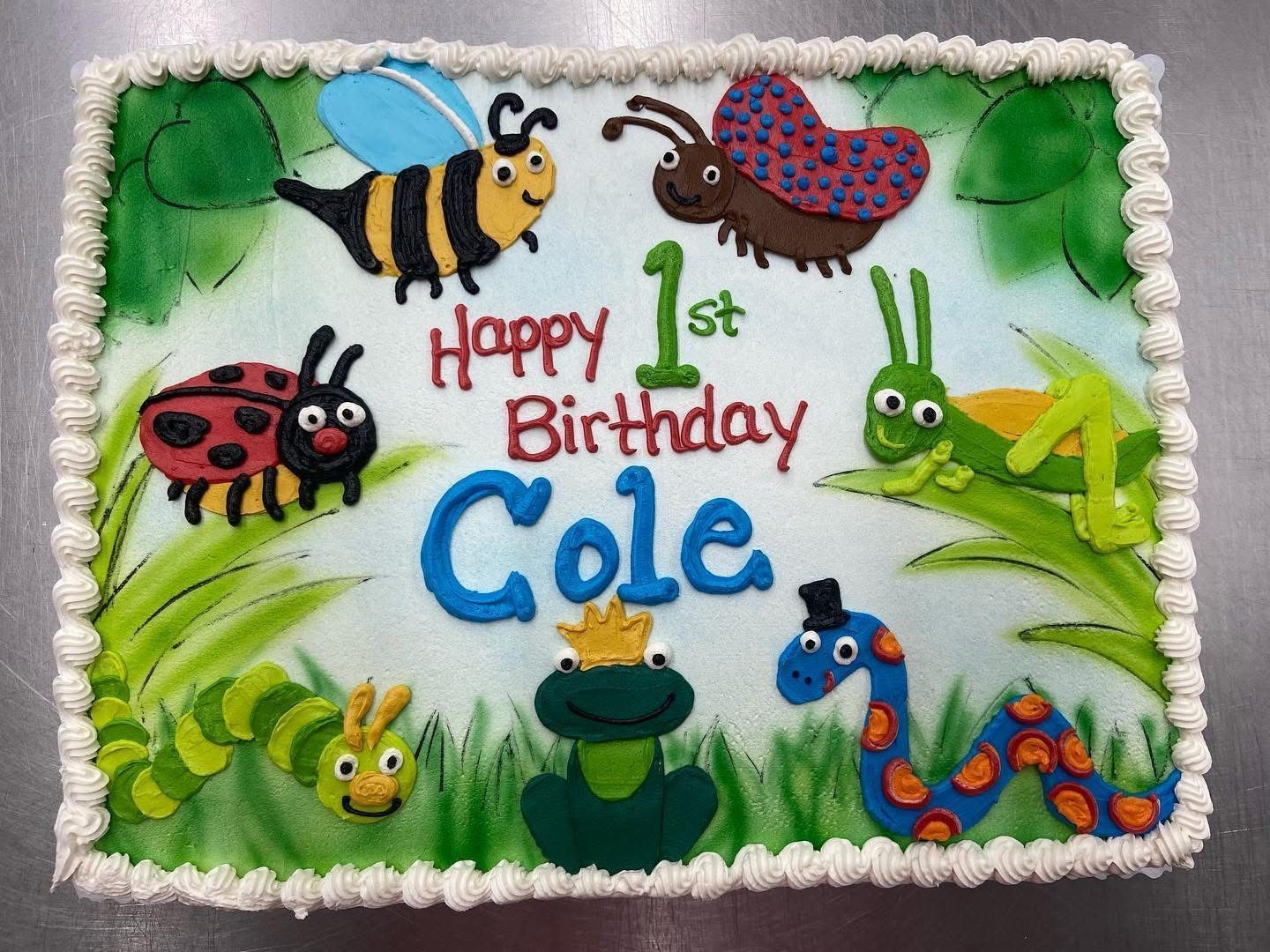 Cake decorated with cartoon insects and Happy 1st Birthday Cole on a green and white frosted rectangle.