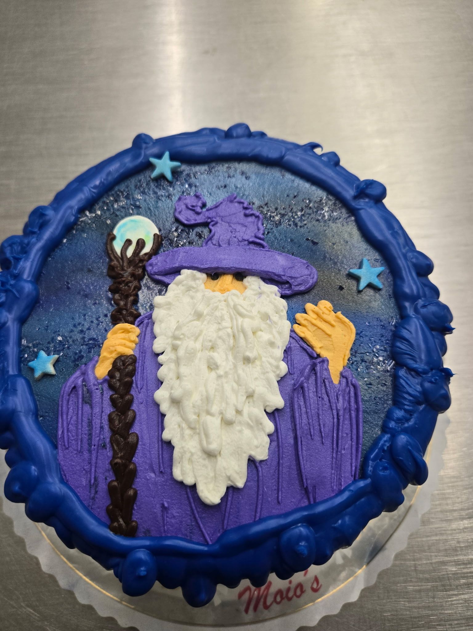 Wizard cake with a blue border, holding a staff, on a silver surface.