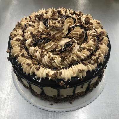 Chocolate cake with tan frosting, drizzled chocolate and sprinkles on a silver surface.