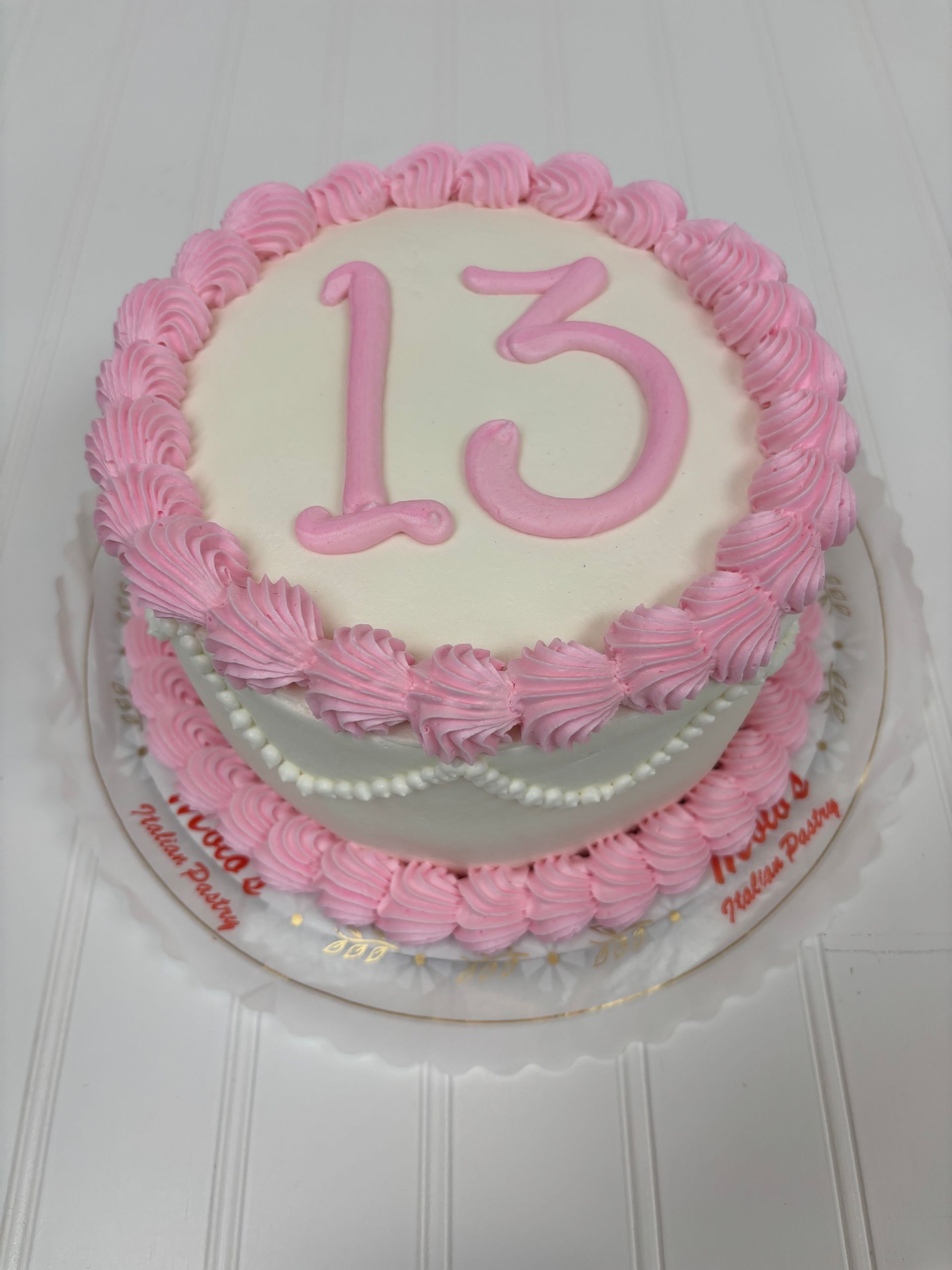 Two-tiered white cake with pink frosting and 13 on top.