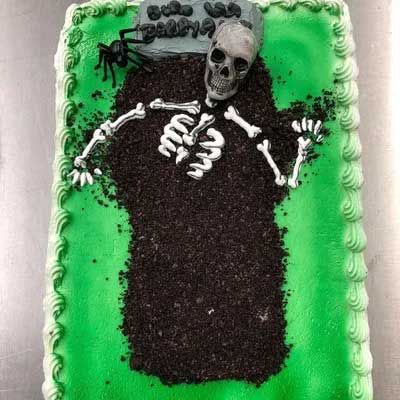 Halloween cake with a skeleton emerging from a grave on a green frosted rectangle.