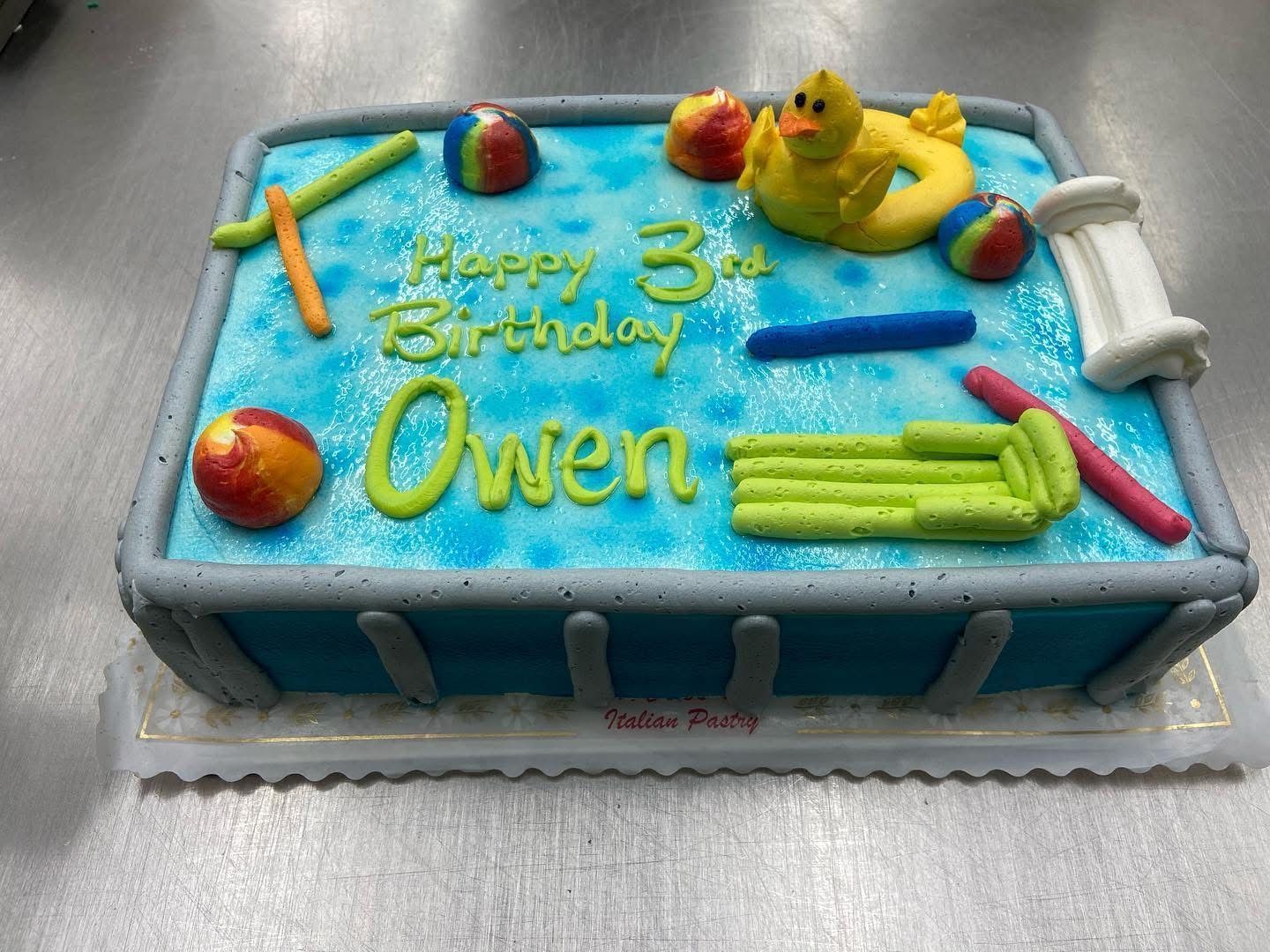 Cake decorated as a swimming pool, blue frosting with pool toys.