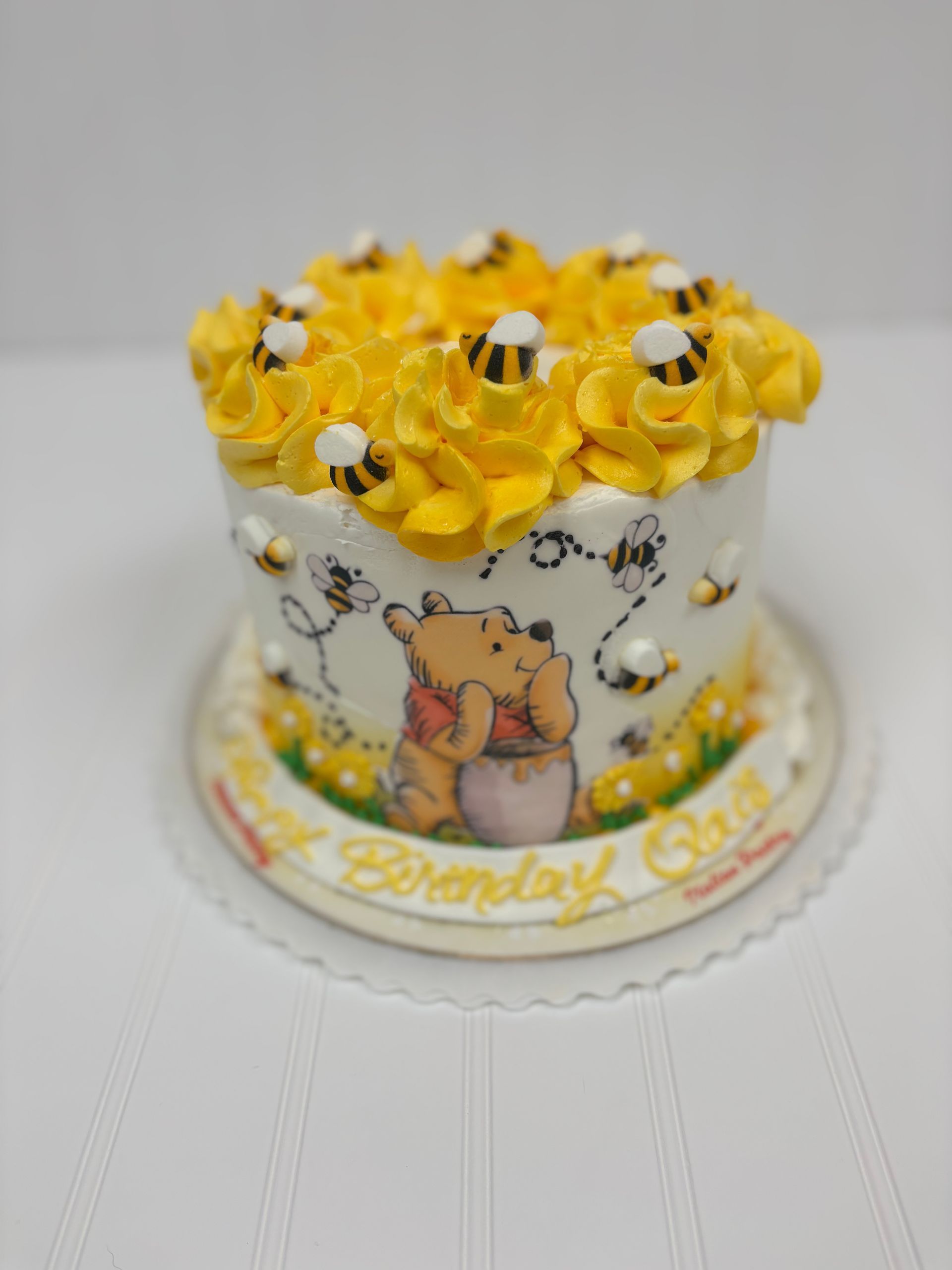 Winnie the Pooh cake with yellow frosting and bees, birthday message around the base.